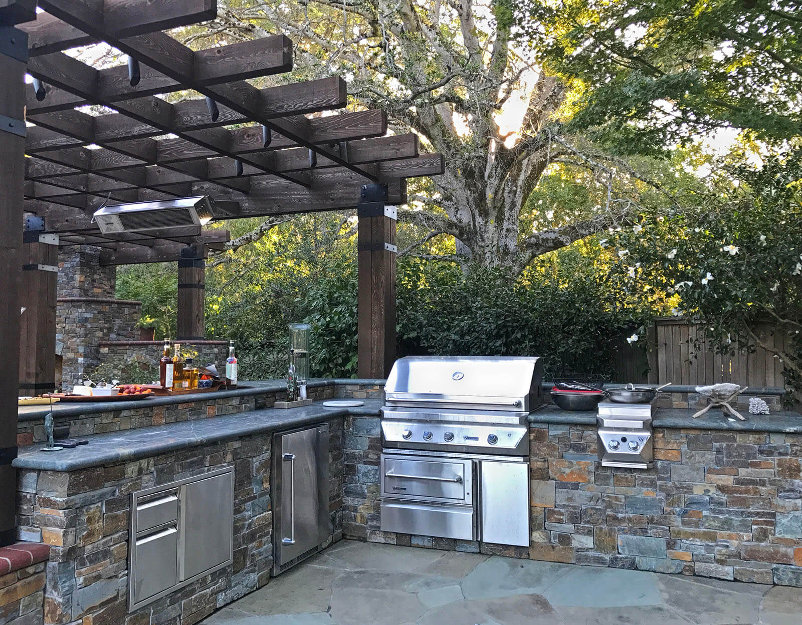 Outdoor kitchen with two-tiered counter and built-in grill adjacent to covered outdoor dining