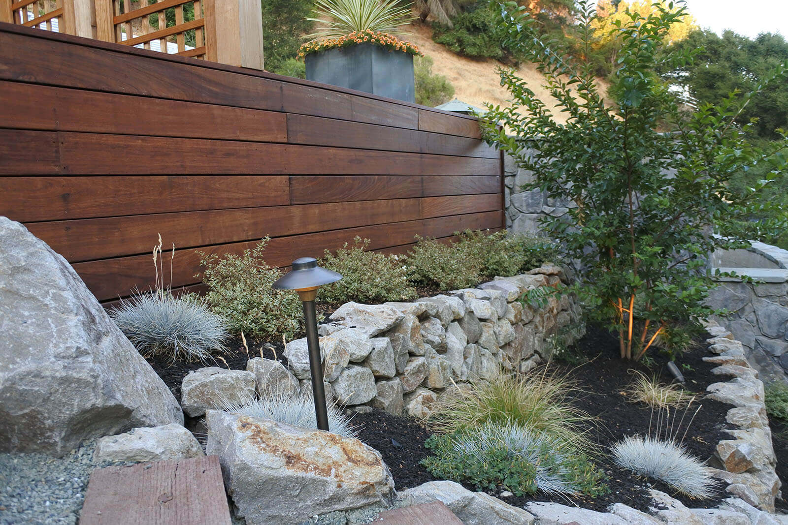 red wood walled backdrop with staged rock wall beds containing short grasses and bushes