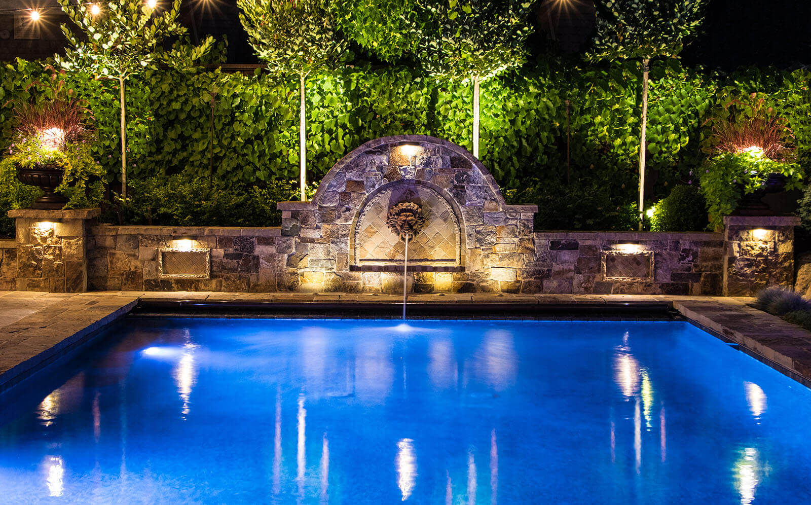Blue light pool with mood lighting around it, and accent lighting for pool fountain and greenery wall
