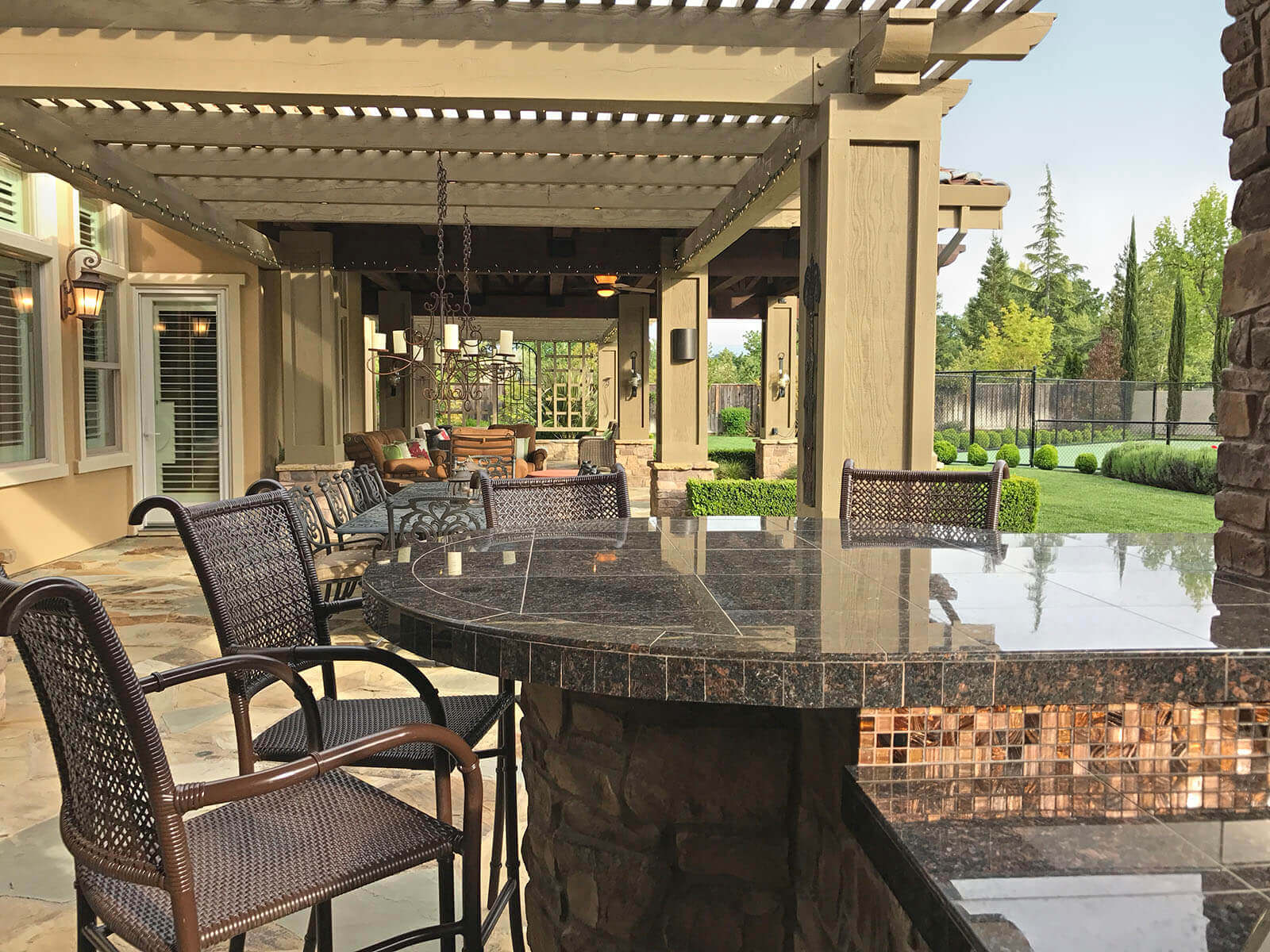 Outdoor dining area with black granite table, pergola-covered lounge, and manicured lawn