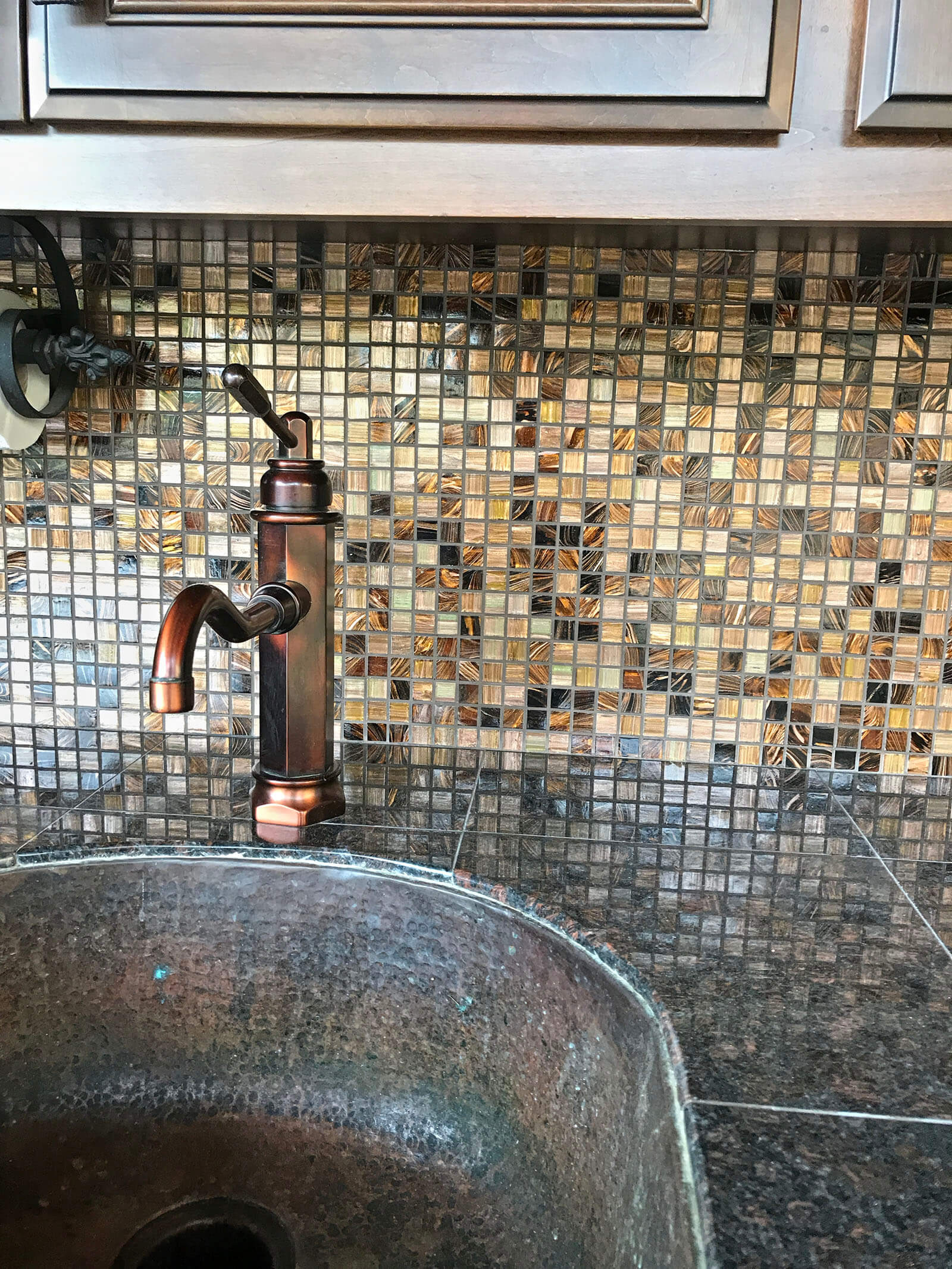 Copper sink fixture with black granite counter tops and mosaic tile backdrop