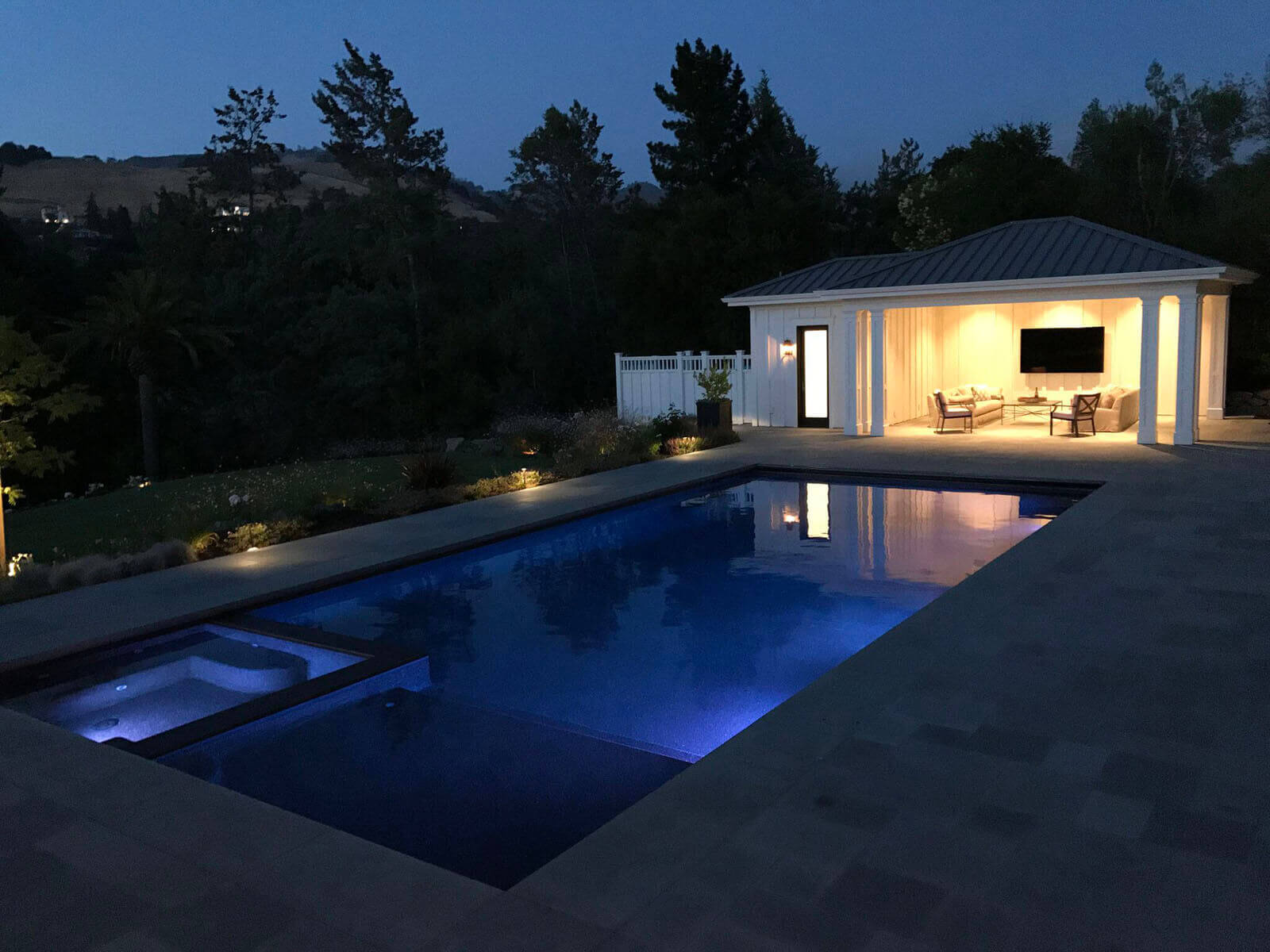 blue lit pool with well-lit covered veranda and accent lighting on the side