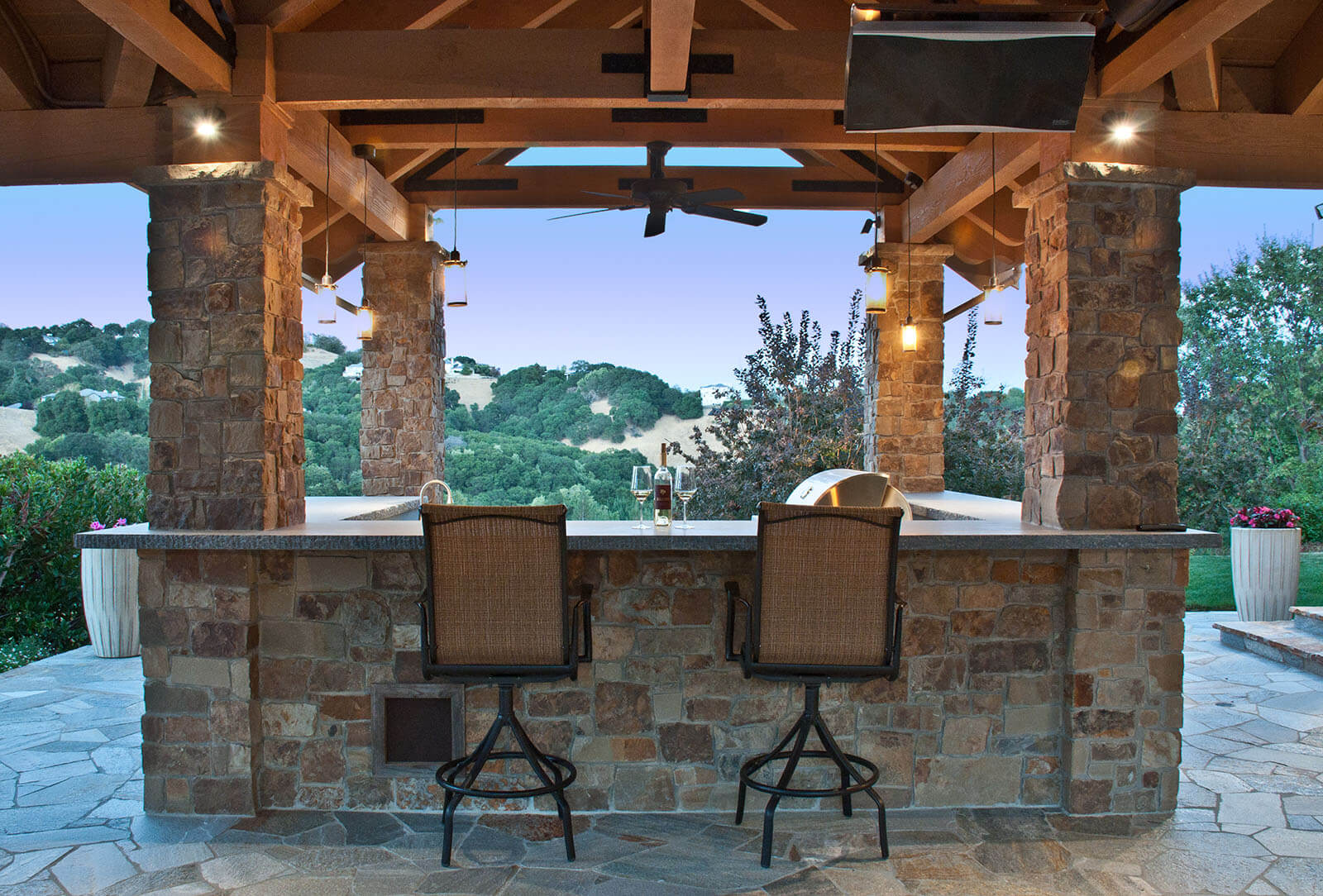 Wood pavilion-covered outdoor bar and grill with stone accents and view of California hills