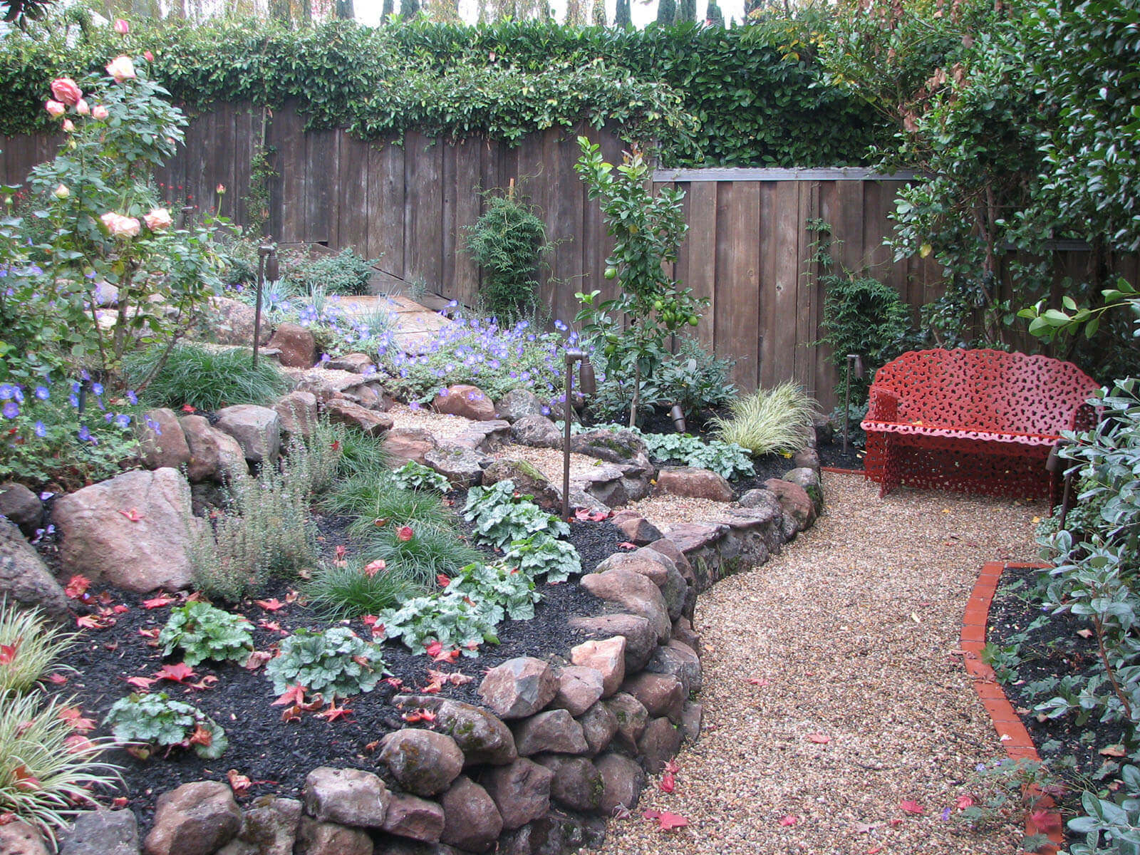 Hillside - gravel and rock walkway with staged garden beds and accented metal outdoor furniture