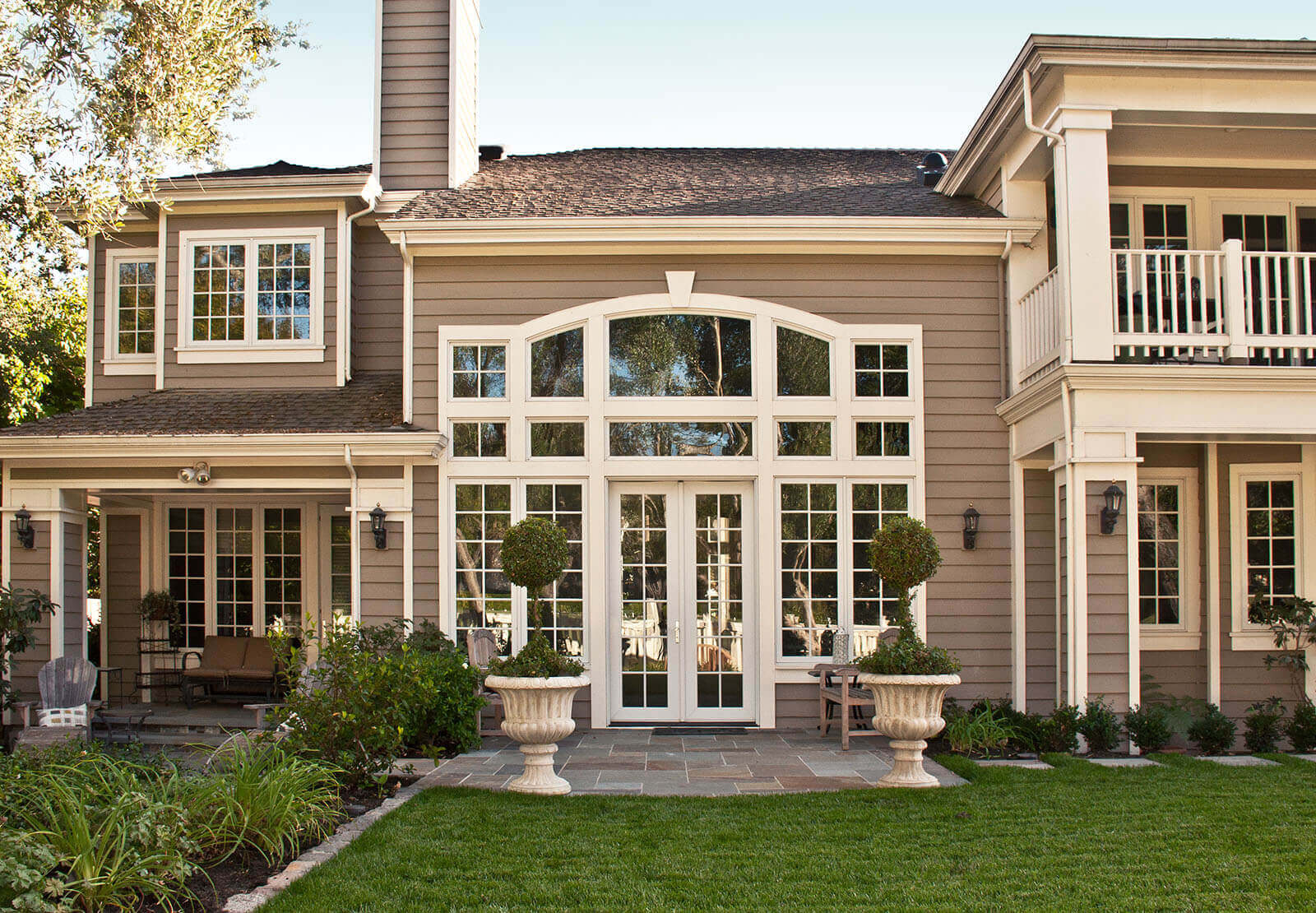 Large windows on back yard entrance with manicured lawn and ornamental stone pots