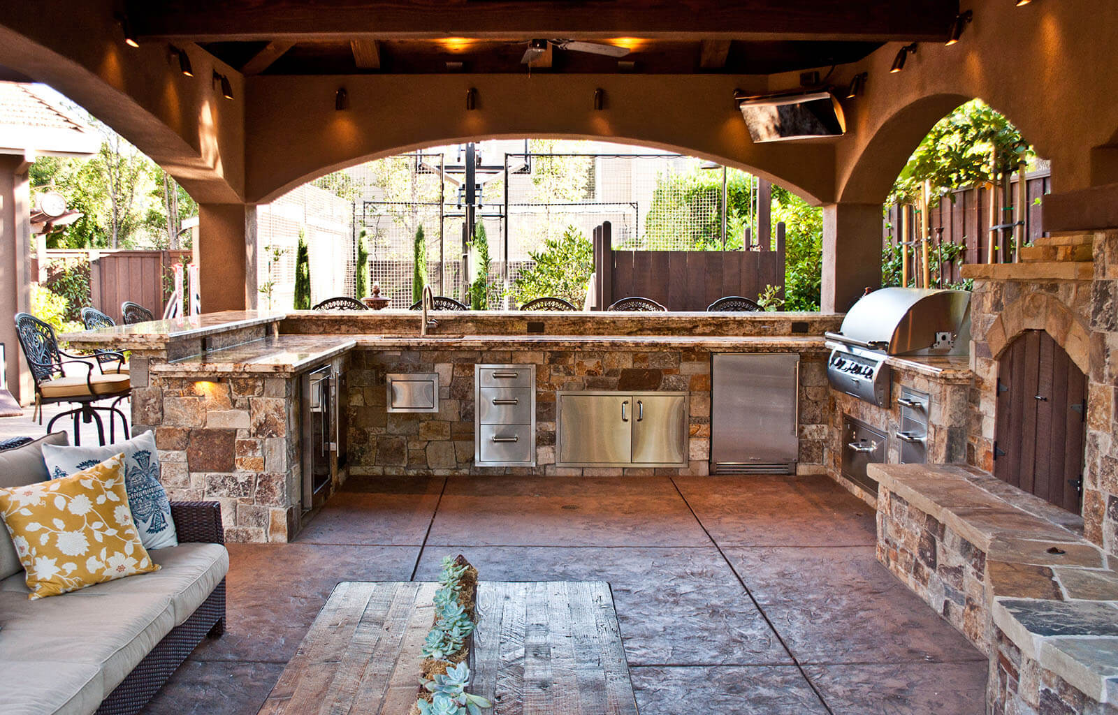 Rustic outdoor covered cooking and grilling area with fireplace and lounge, bar seating, and accented archways