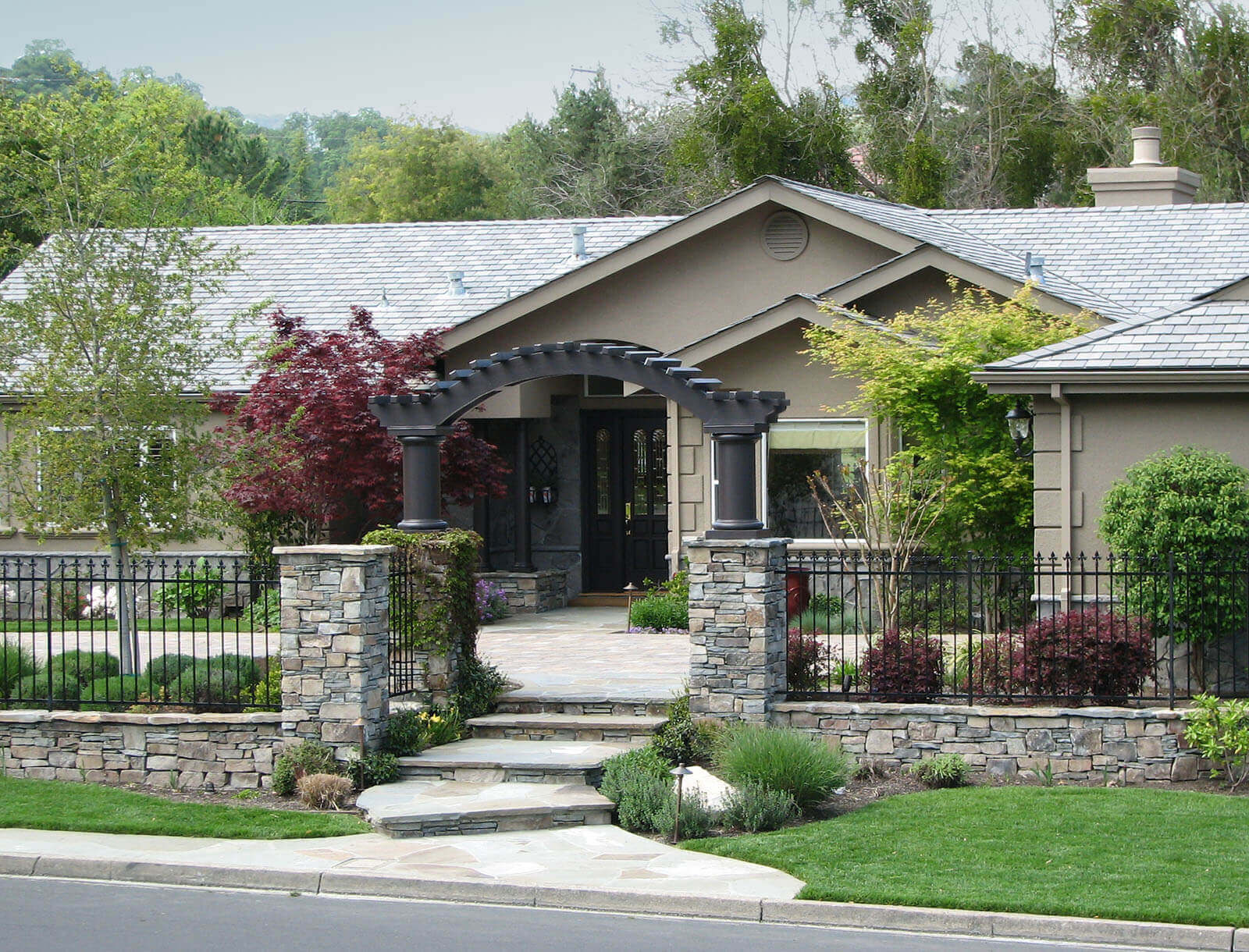 Wrought iron and stone border fence with custom arch and path to entry