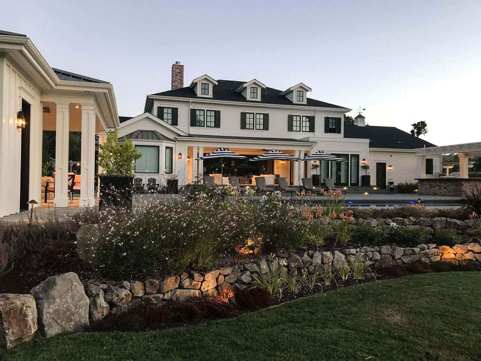 Outdoor lighting at sunset, light fixtures around the edge of the structures, and accent lighting on staged gardening areas