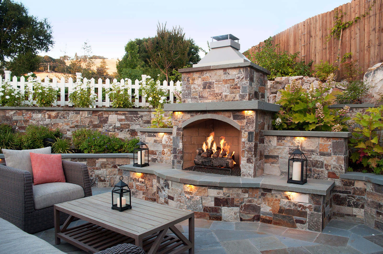 Stone and brick outdoor short fireplace with large hearth, next to lounging area