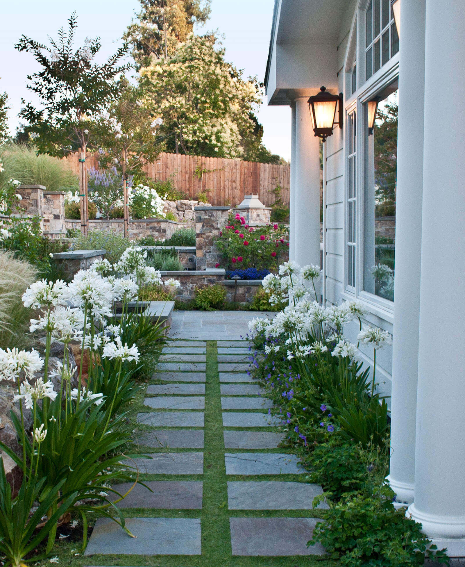 two row square tile walkway leading through side yard, lined with flowering plants