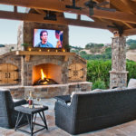 Outdoor covered heated patio with large stone fireplace and wood storage with rattan furniture