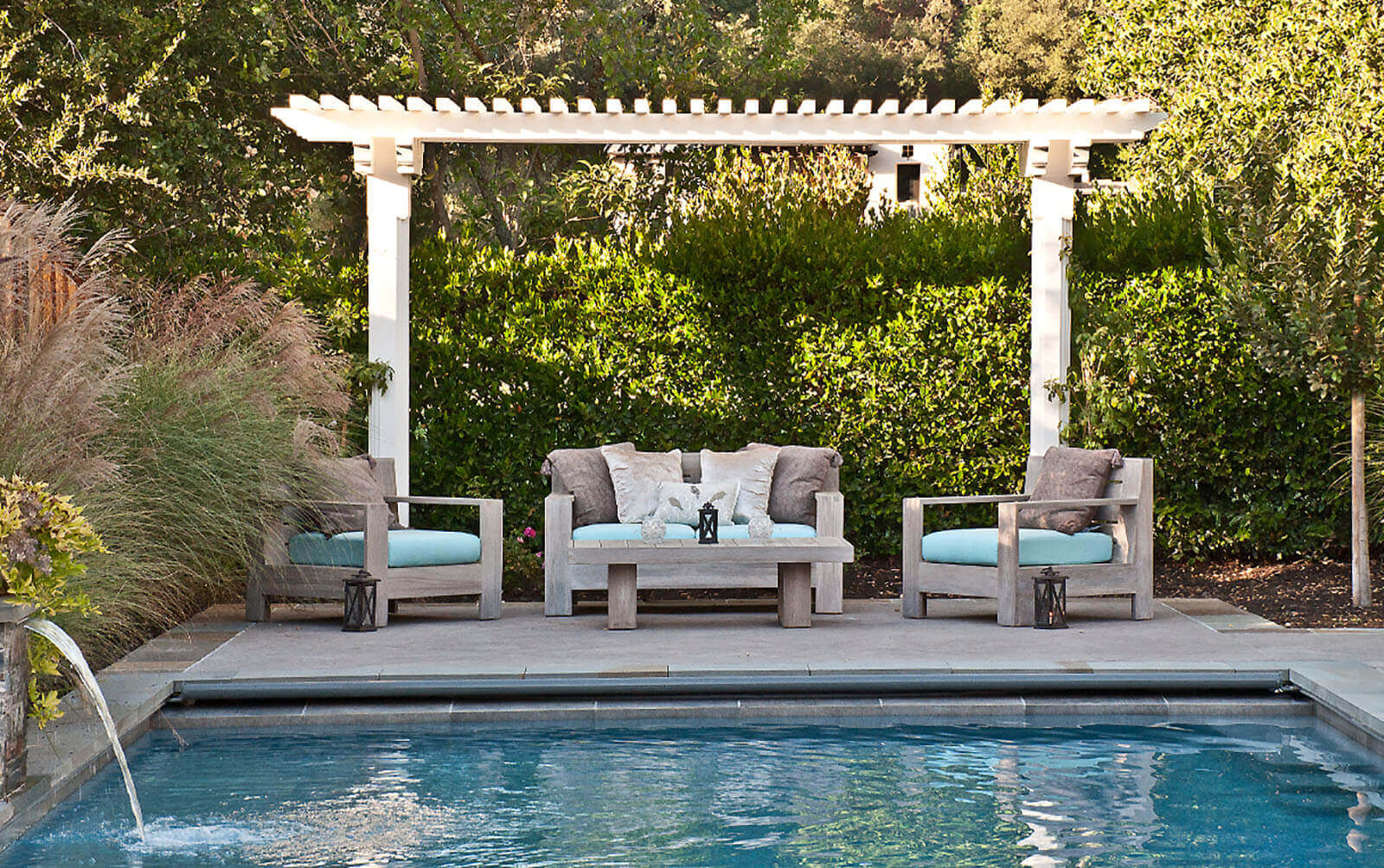 Classic white pergola shades a poolside seating area with backdrop of lush screening hedge