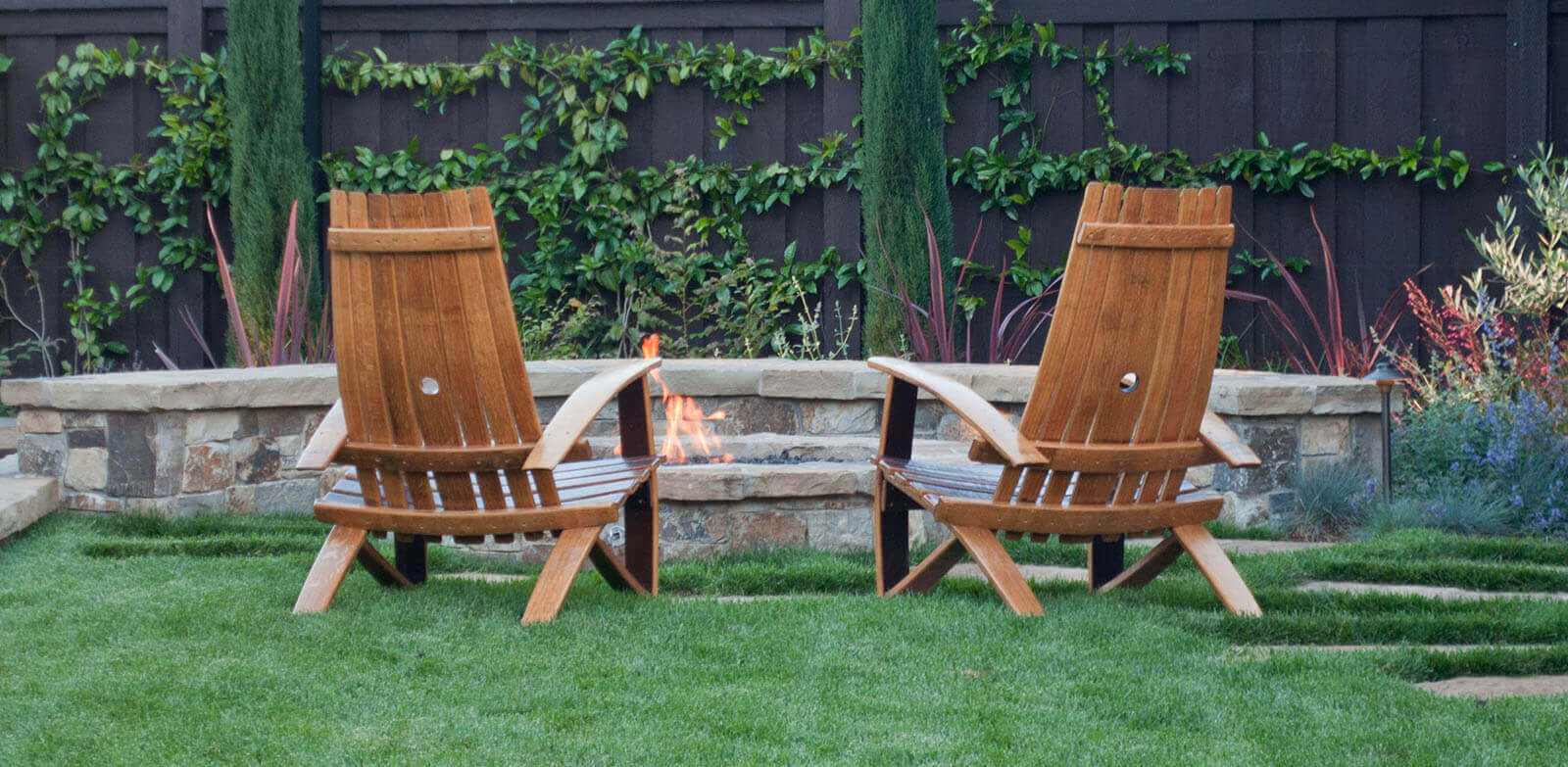 Low round firepit set in lawn with Adirondack chairs and low stone seat wall