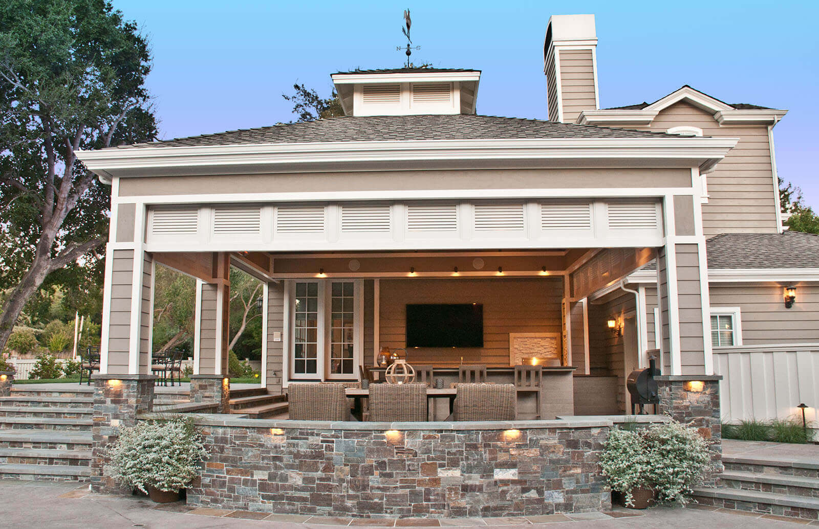 Contemporary farmhouse-style pergola shelters outdoor dining area with stone details and landscape lighting