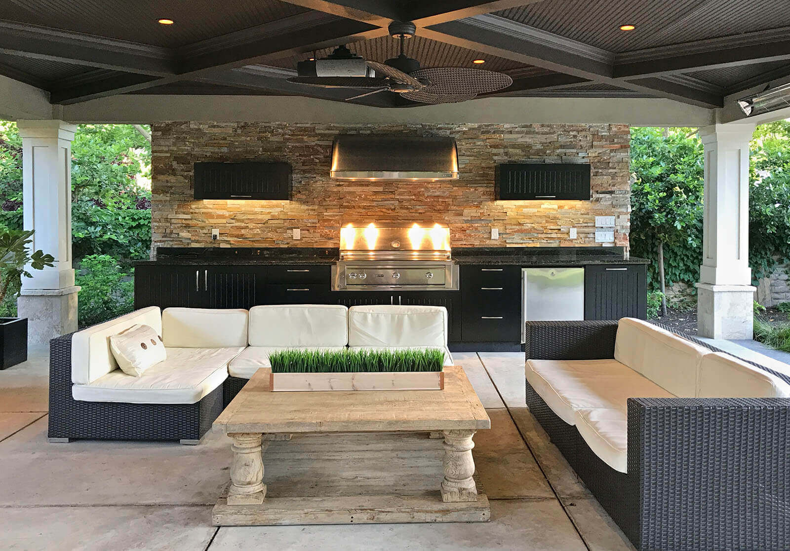 Warmly lit outdoor lounge with dark contemporary ceiling and outdoor kitchen with stone details