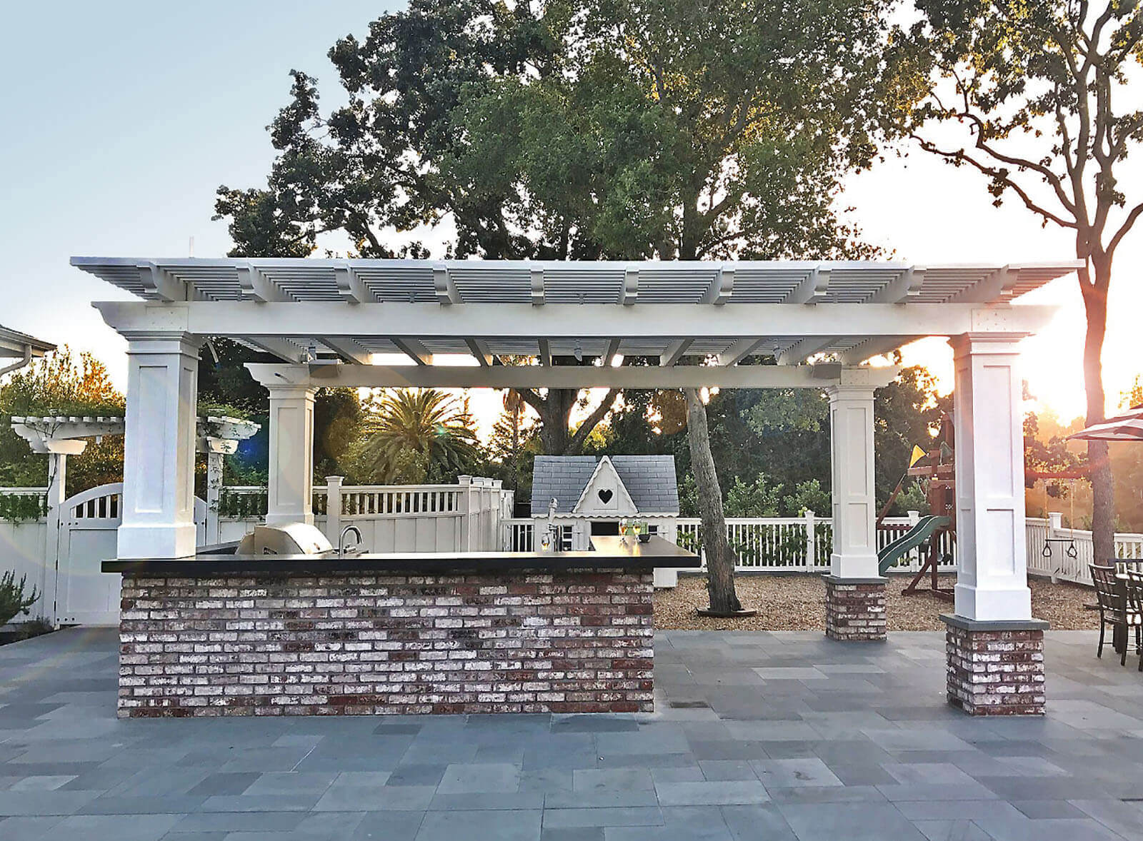 brick, stone and white column pergola with black counter tops and brick walled bbq cooking area with sink