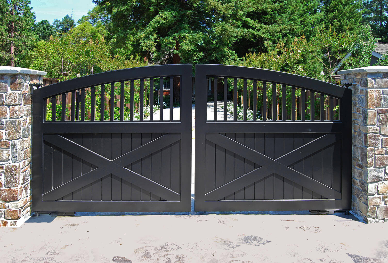 Stately black double gate with stone pillars opens onto a tree-lined drive