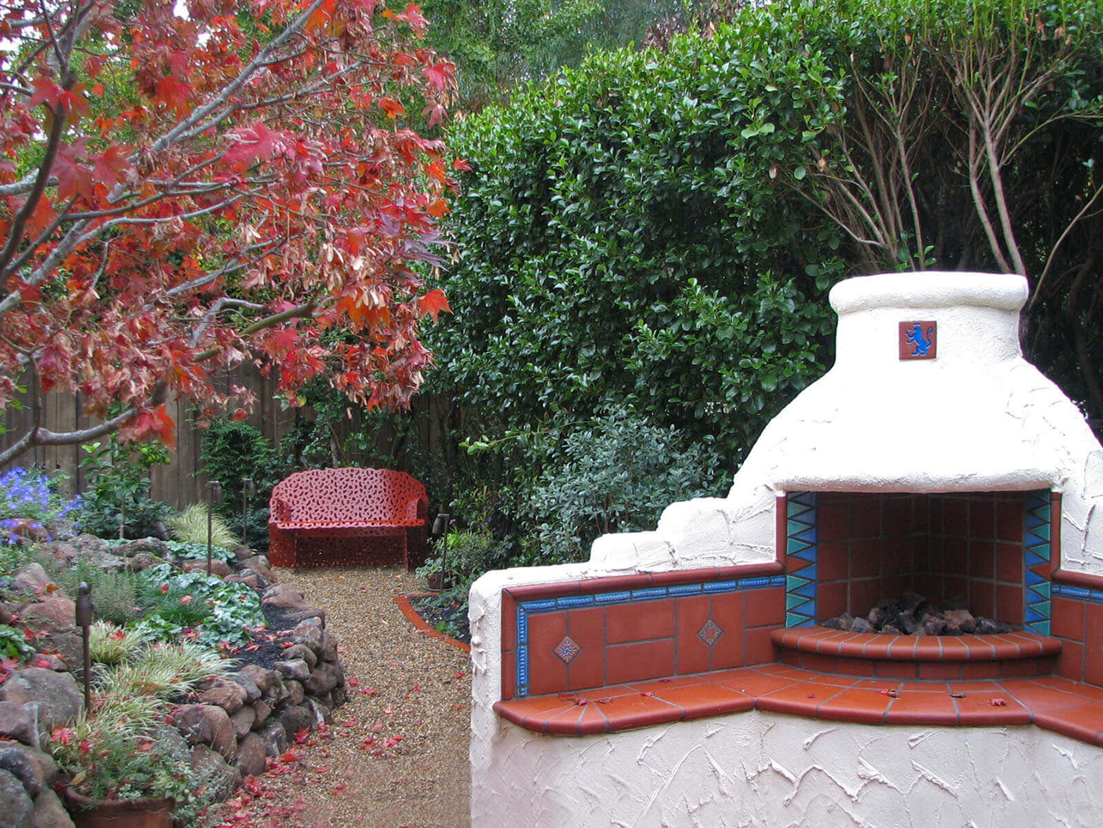 Mission-style stucco fireplace with tiled hearth and red accents in an autumn landscape