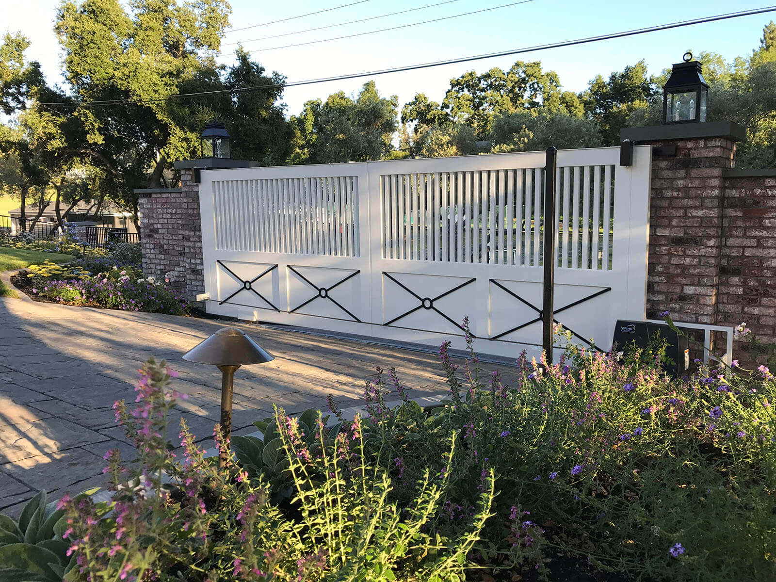 tall ranch style slatted driveway gates with brick posts and side wall with surrounding wrought iron fencing