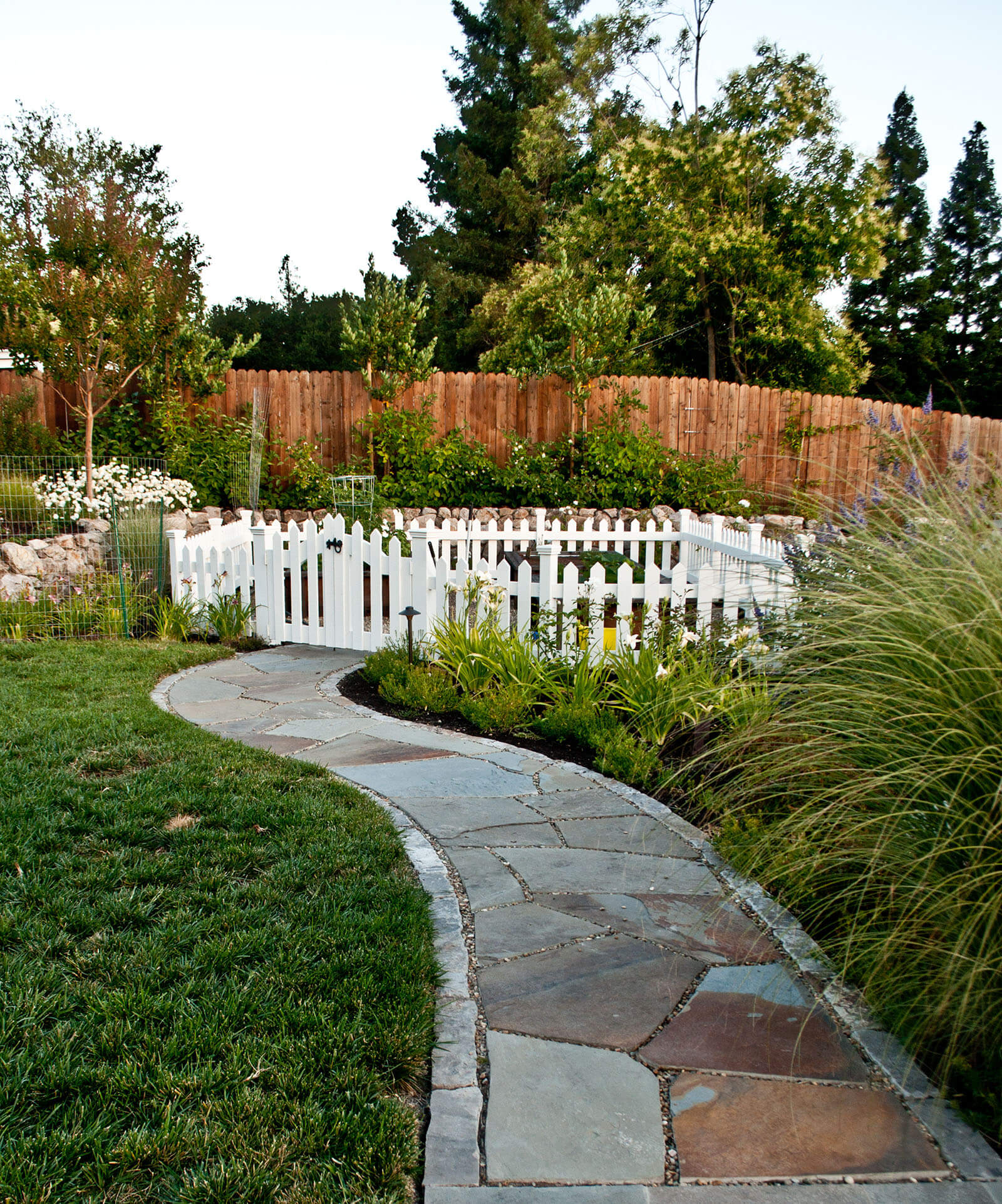 Stone walkway leading to white picket fenced gardening area