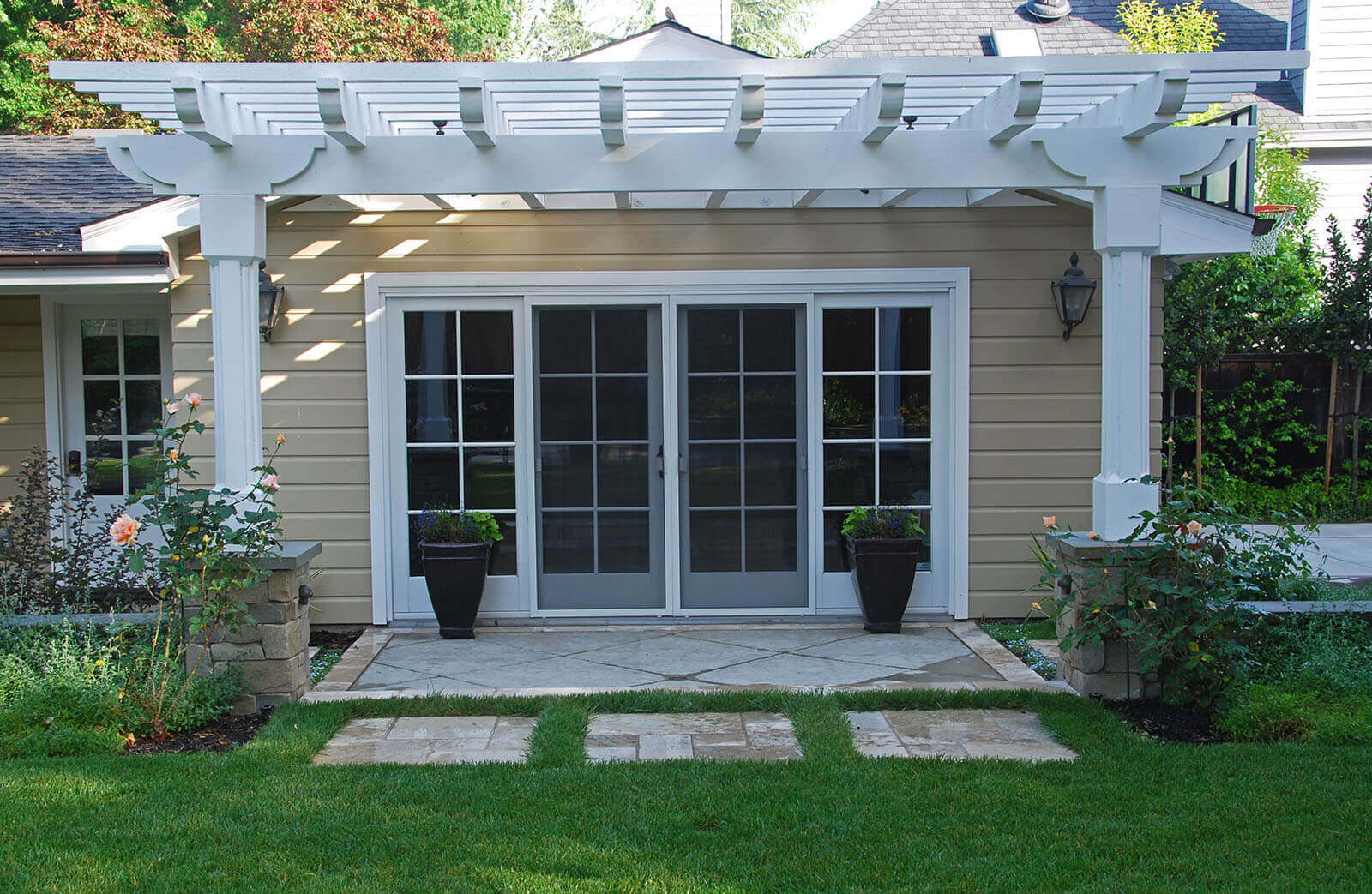 Classis white wood veranda shelters a contemporary concrete and stone patio entry set in a lush lawn with climbing roses