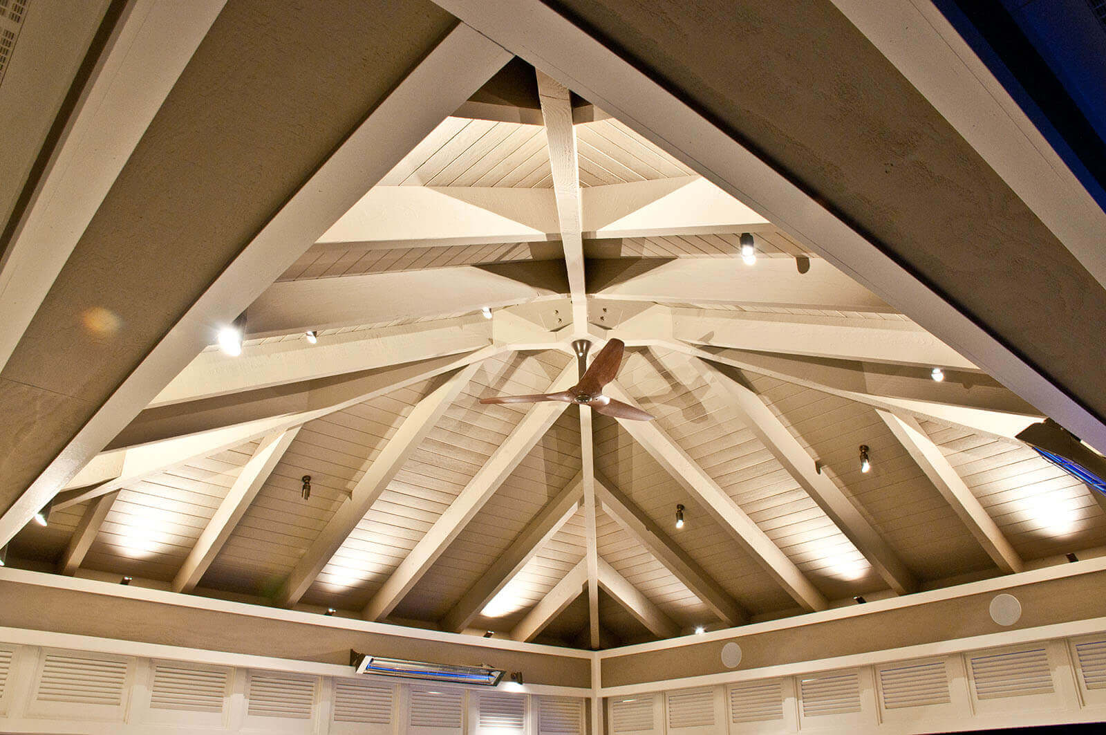 Interior shot of light accented pyramid wood roofing and fan with heating and lights below