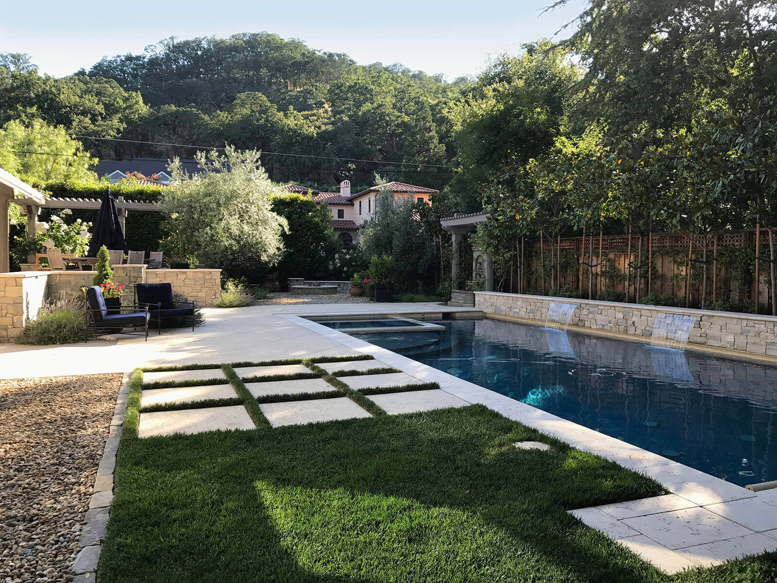 Shaded lap pool with sheer descent falls bordered by contemporary stone patio and lawn