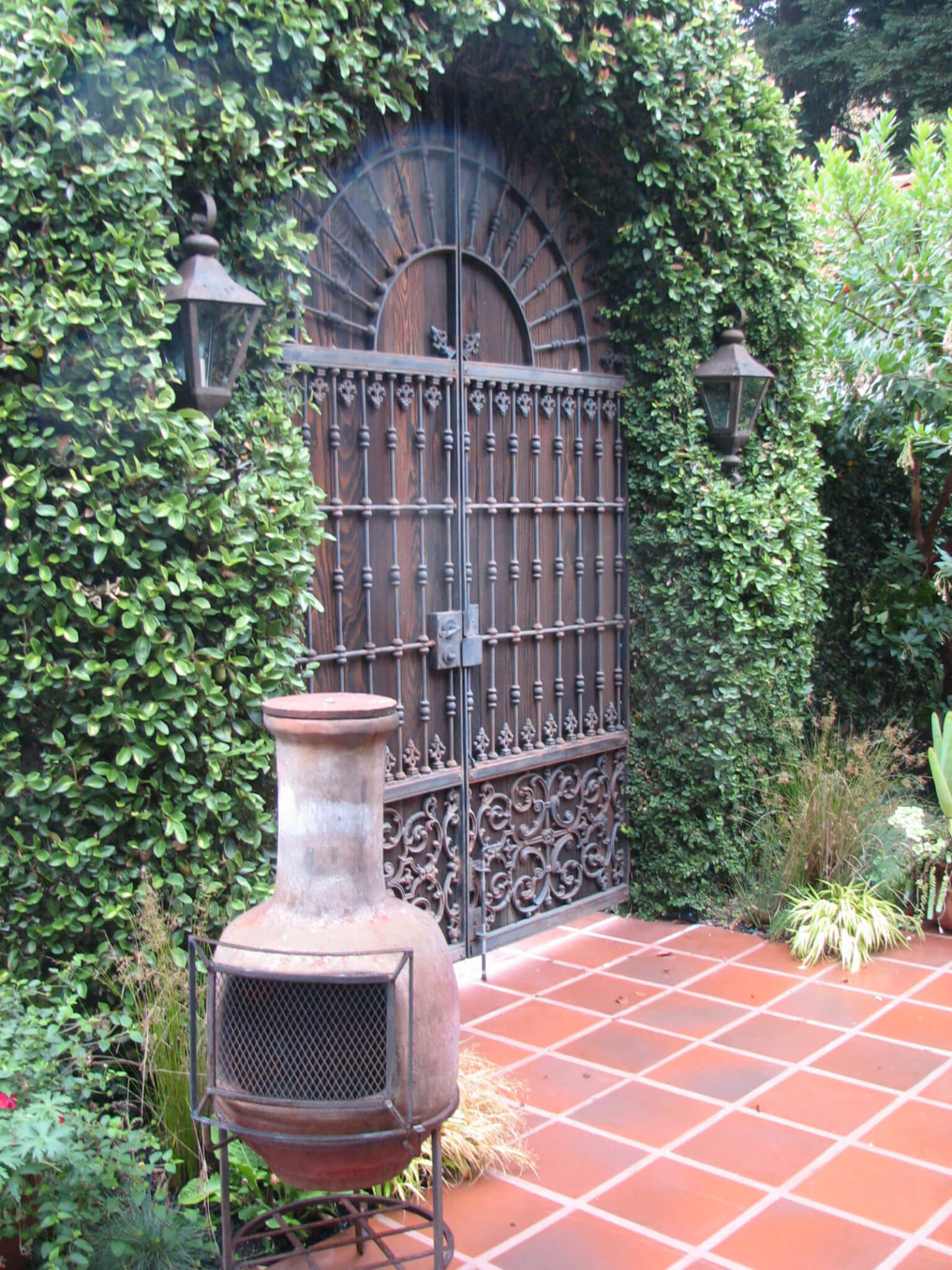 Rustic iron and wood doors set in vine-covered wall opens into a Spanish style courtyard