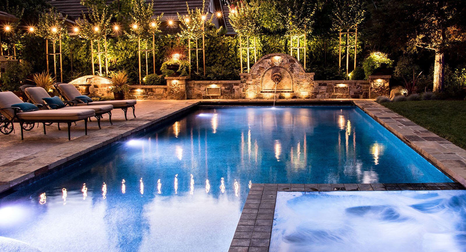 Elegantly lit pool in stone patio with lion's head fountain