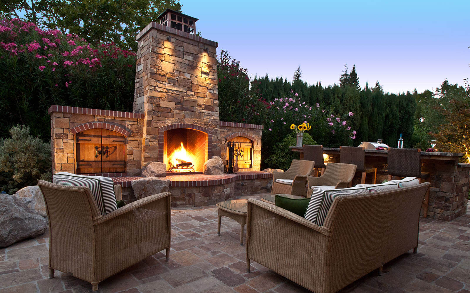 Stone and brick fireplace with rustic wooden details on a stone patio with outdoor lounges
