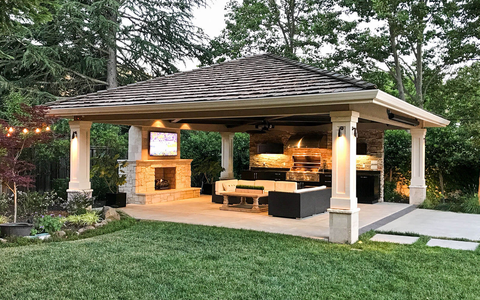 Pyramid-roofed pergola protects an outdoor living area with kitchen, bar, lounge and fireplace on a contemporary concrete patio