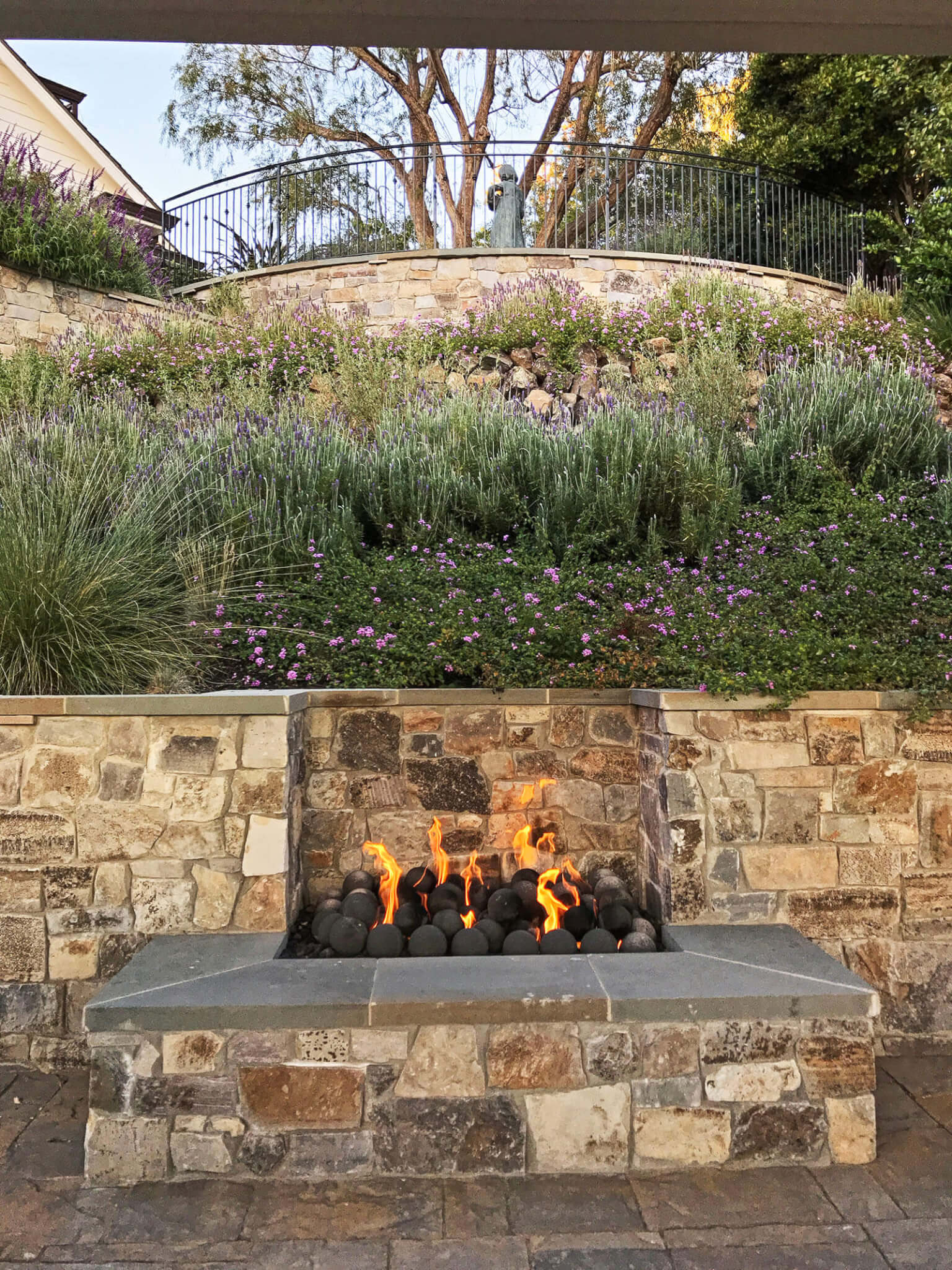 Outdoor stone tile fireplace with round fire stones and elevated sloped garden