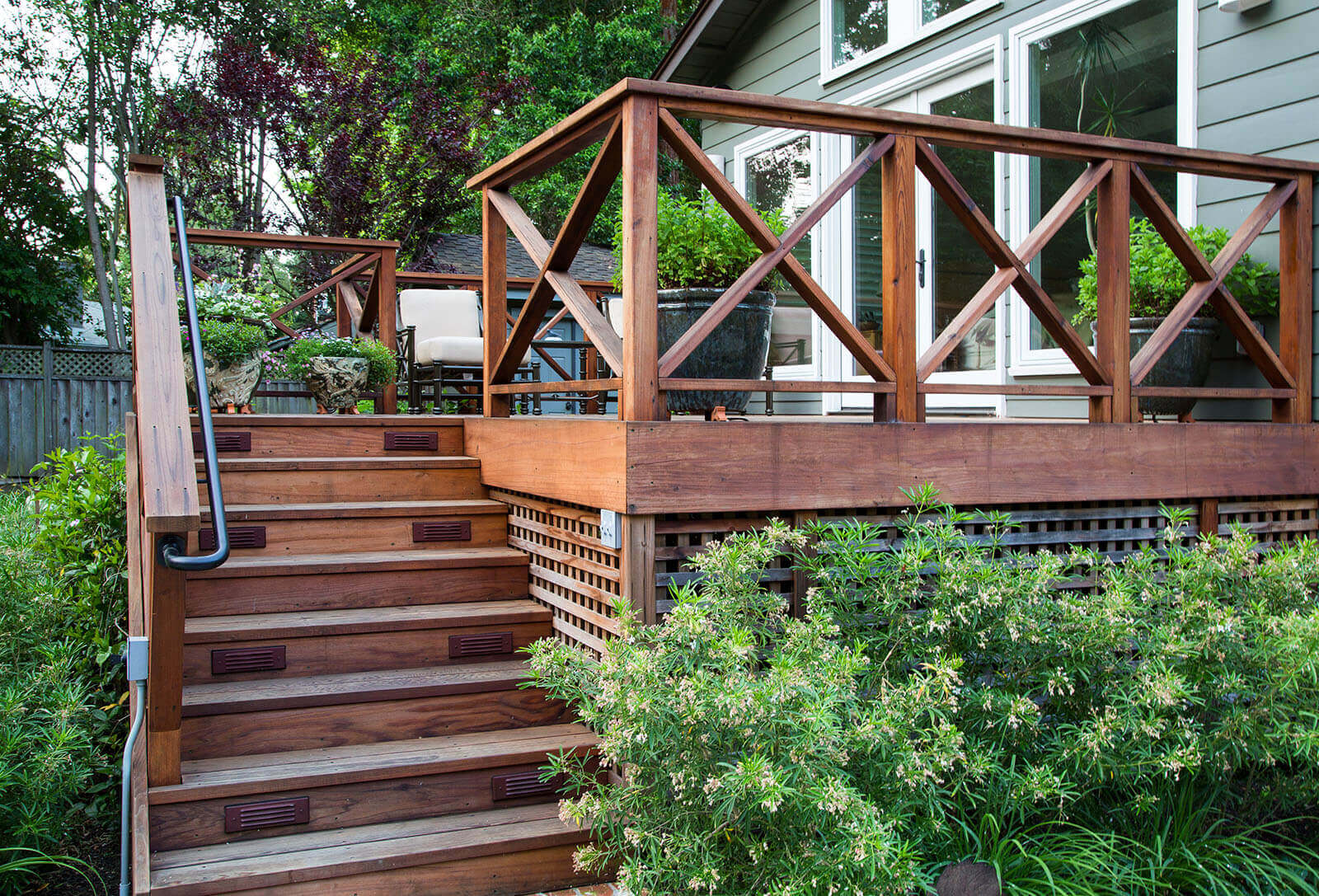 wooden lattice base elevated dark wood deck with dark wood stairs, and railings leading from greenery in the yard