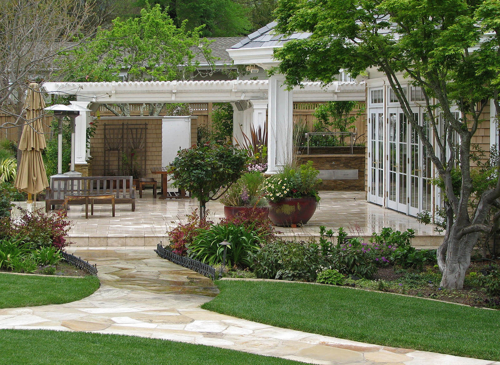 large elevated white stone patio sporting rustic wooden furniture, ornamental ceramic pots, flower beds with a white stone path going down the middle