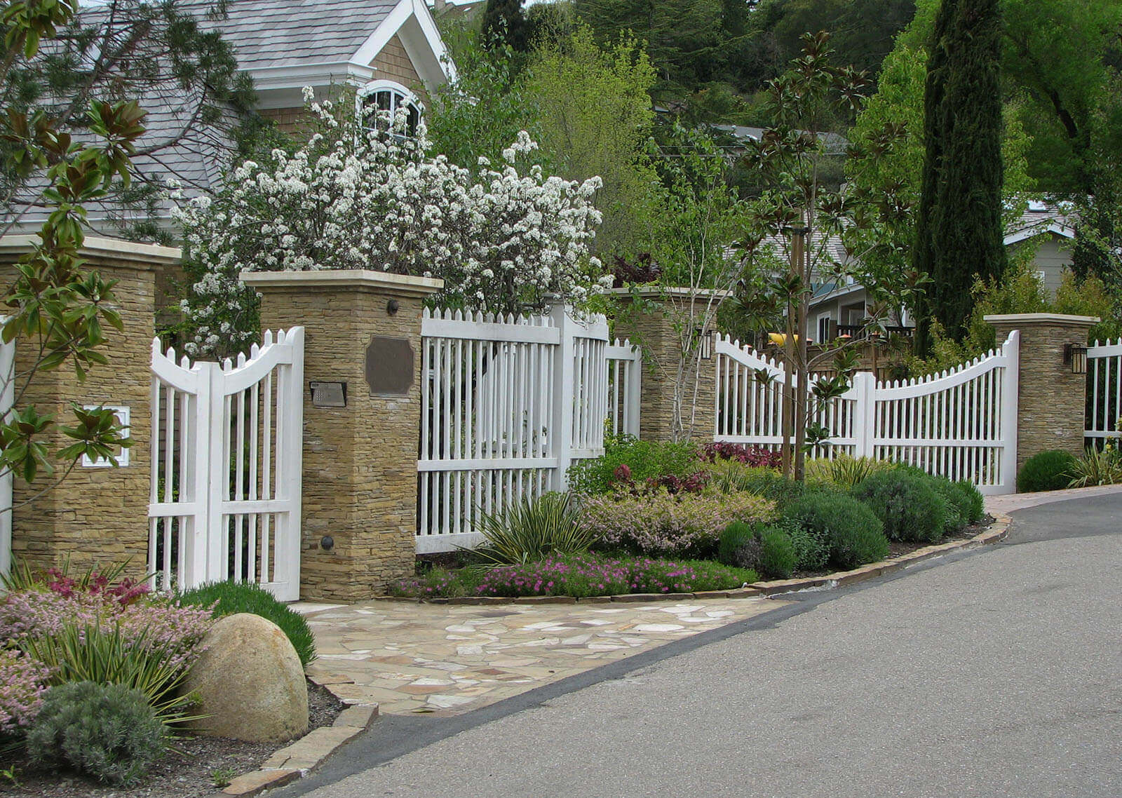 Tall scalloped fence with stone pillars and curb appeal planting