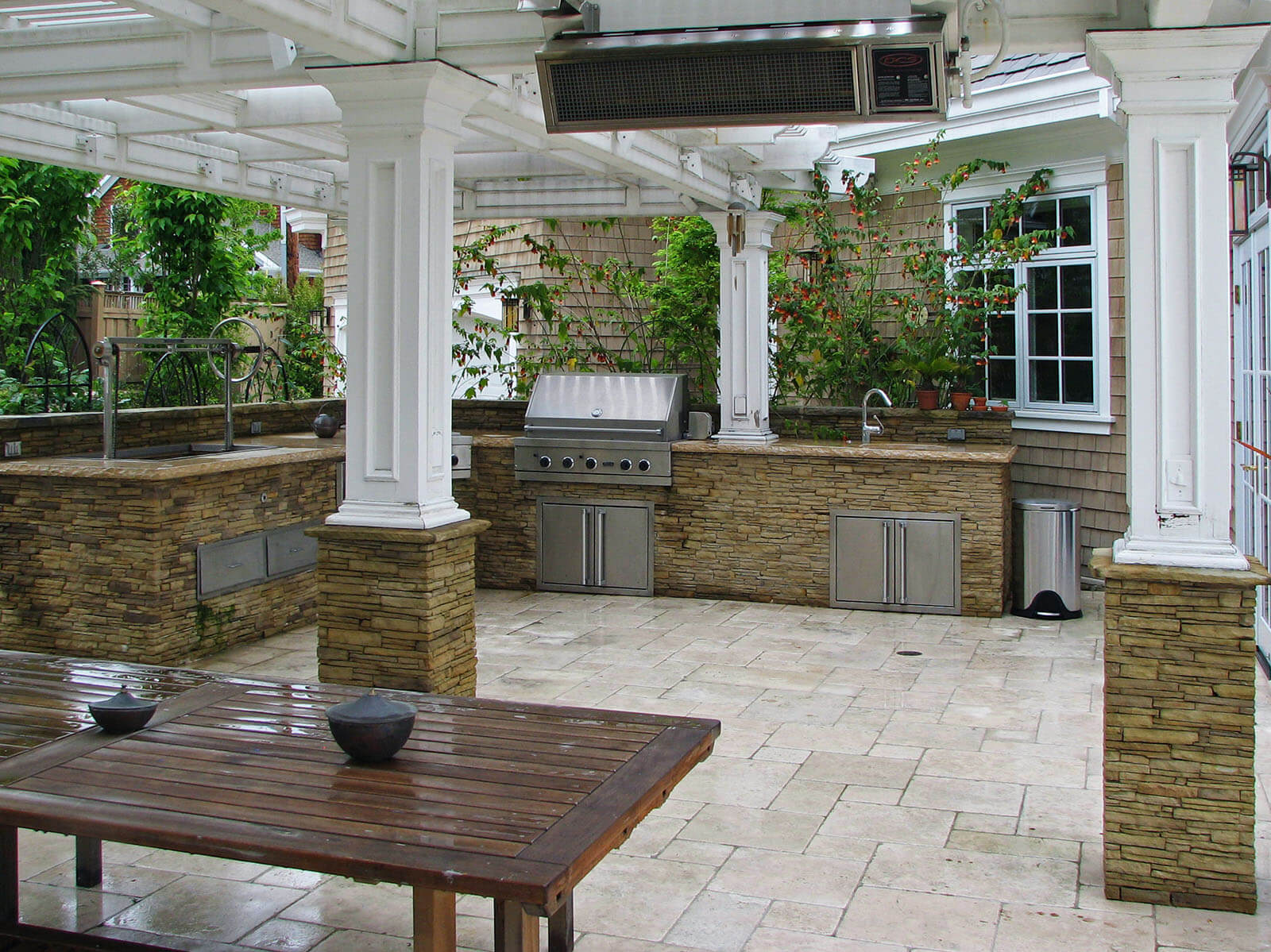 Heated white tile patio with pergola roofing and wide bbq kitchen area with rustic table set