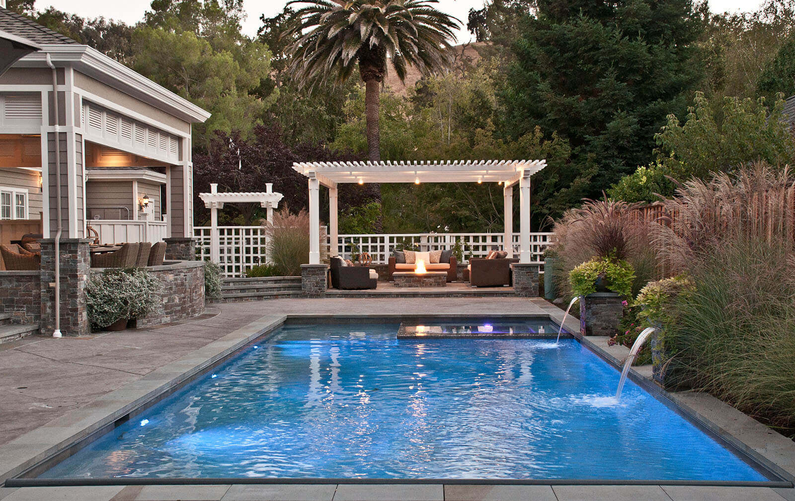 Zero-edge pool with inset spa and sheer descent falls with poolside lounge and planting