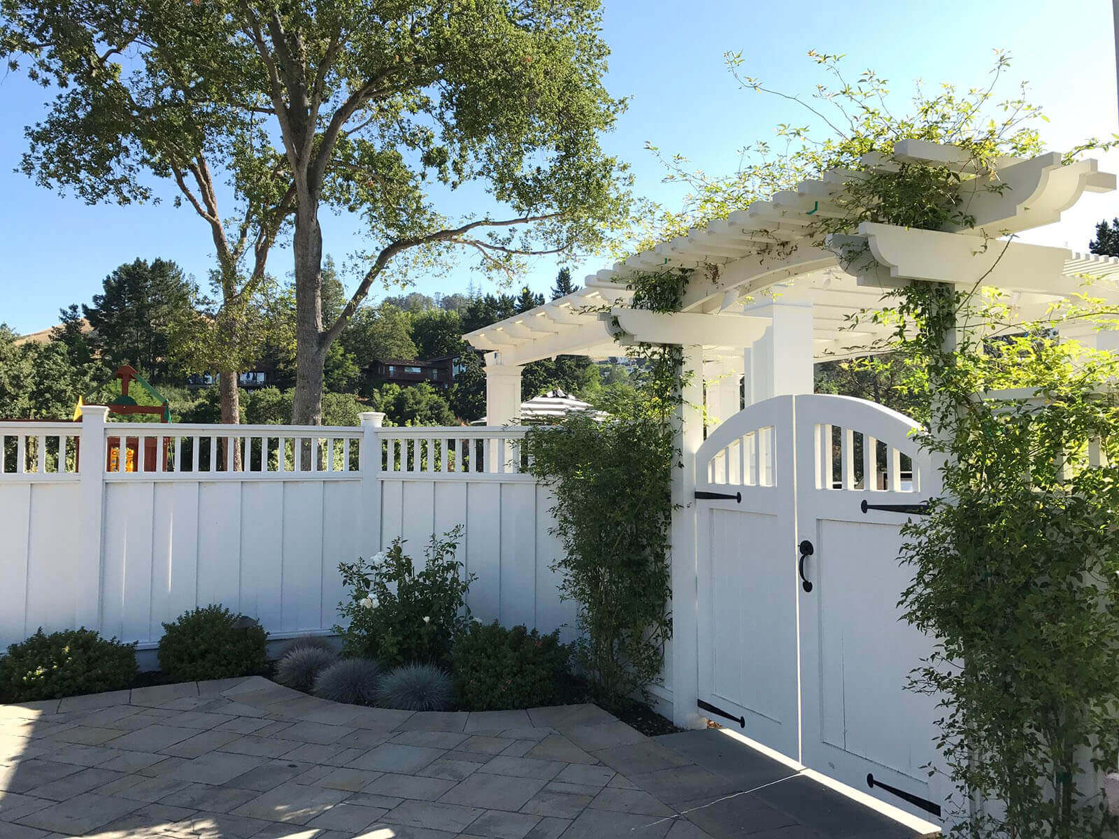 Tall white custom fence with arbor gate featuring wrought iron hardware
