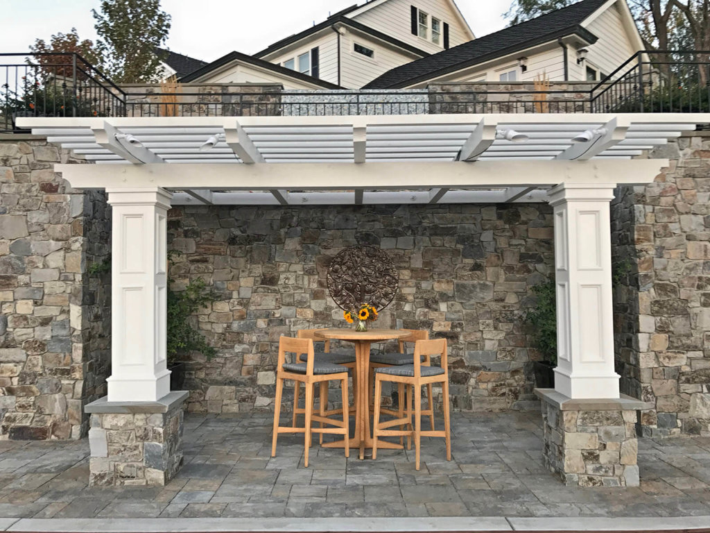(side view) shaded resting area with ornate metal wall fixture and wooden furniture on stone patterned tile patio