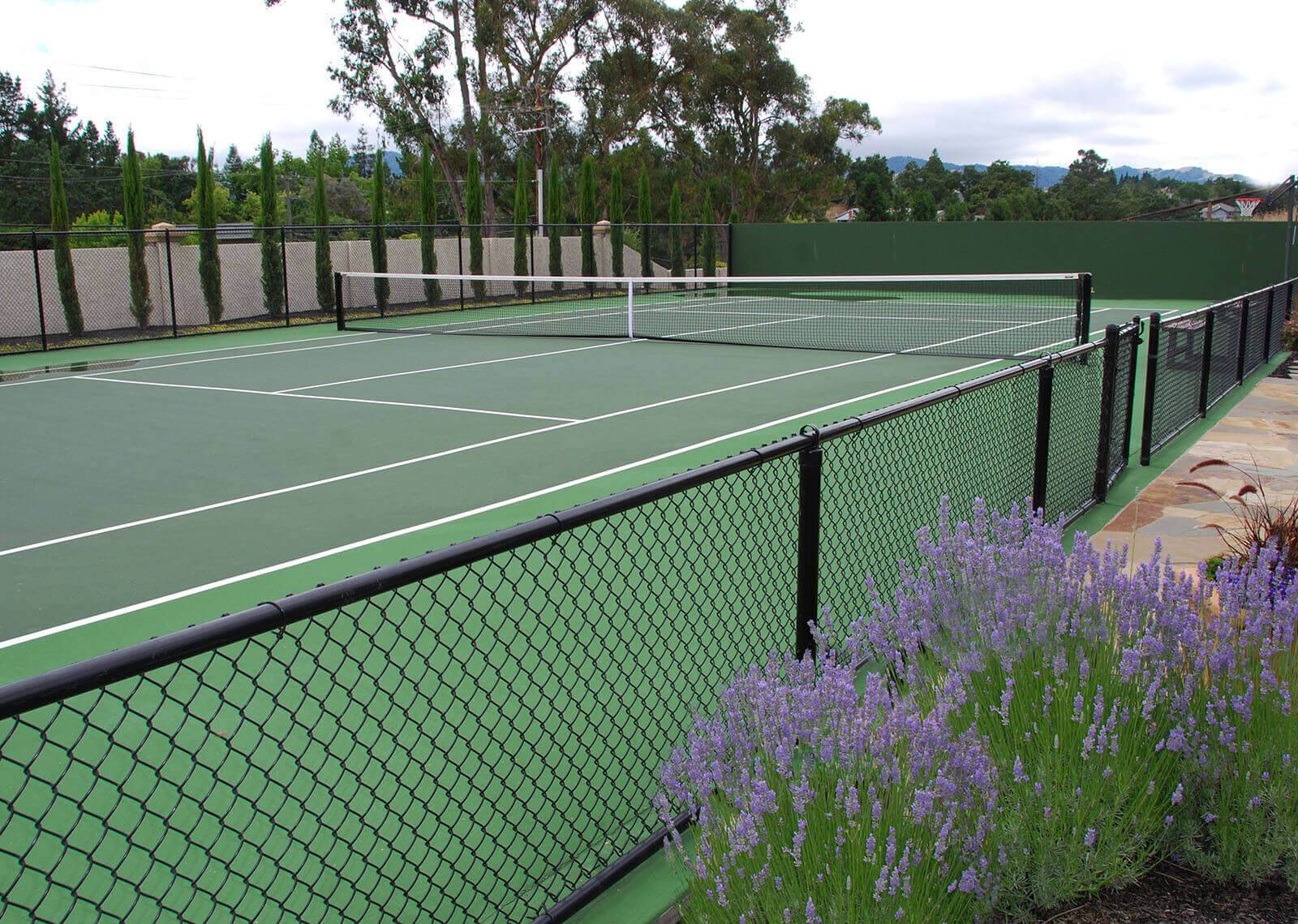 low fence private tennis court with stone walkway and surrounding greenery and lavender