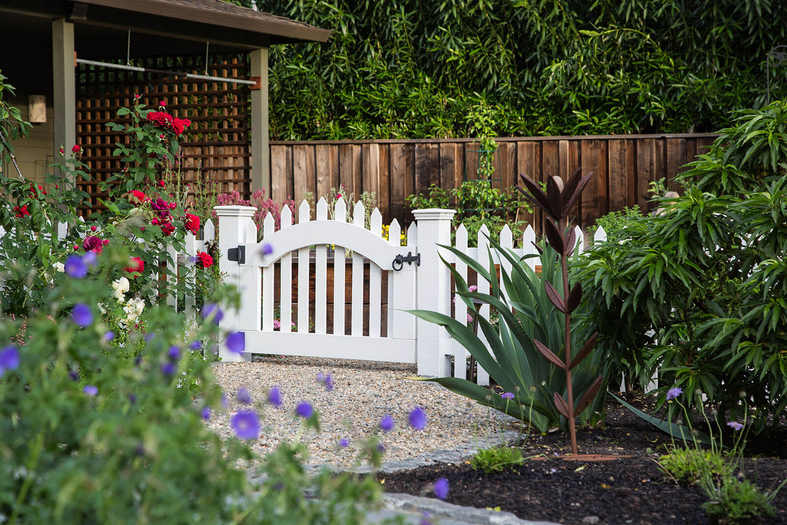 White picket fence bordered entrance to gardening area with shaded trellis