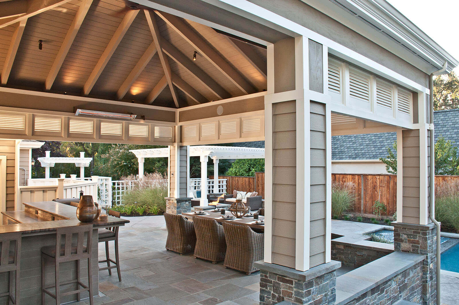 Pyramid-roofed pergola with slatted sun-shades covers outdoor bar and dining area on bluestone patio