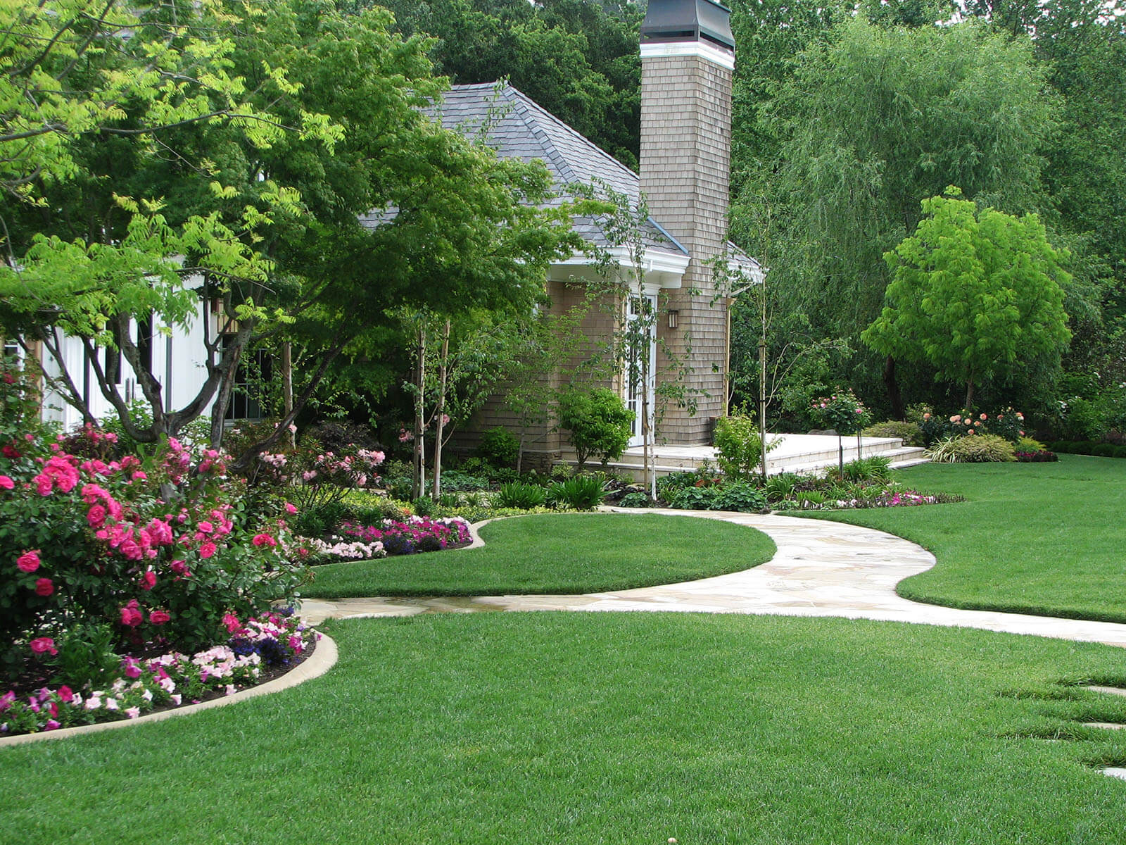 Curvy white stone pathways carving through manicured short lawn, going to various entrances around the house, like a staged white stone deck with stairs