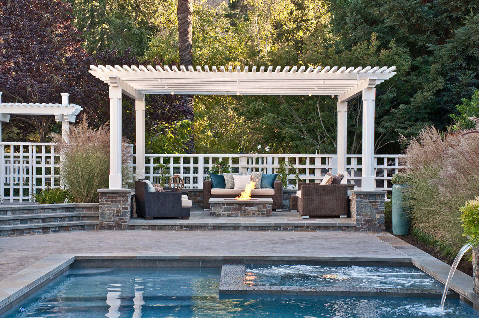 Poolside patio with rectangular gas fire pit and lounge area under a white pergola