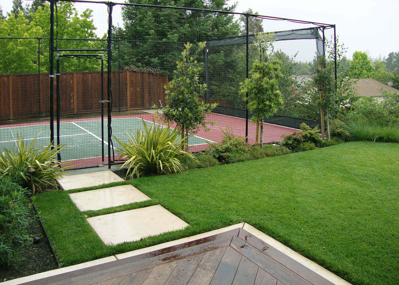 white tile-lined wooden deck with short stairs, and white stepping stones to fenced tennis court