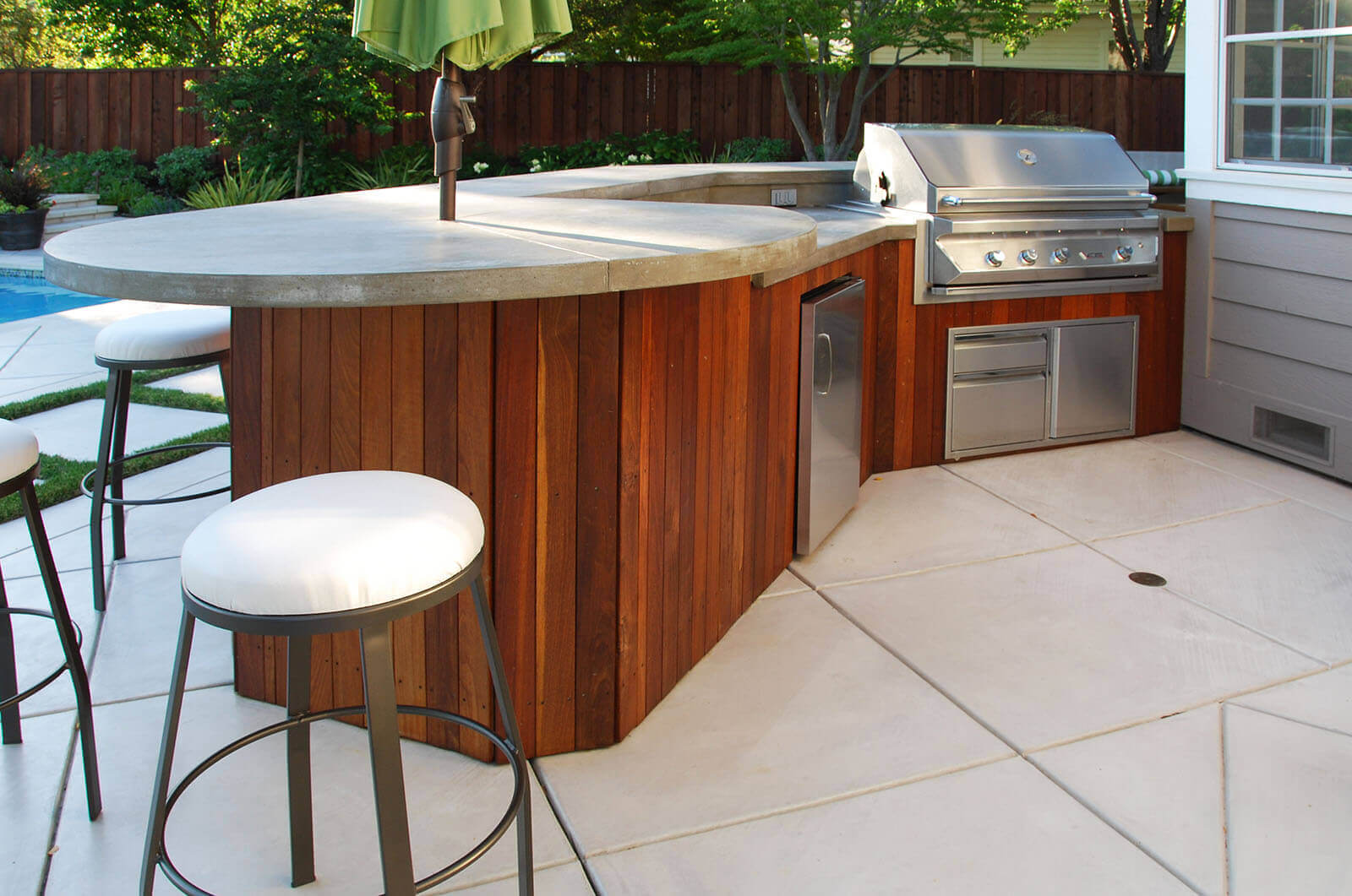 Stone tile counter top with center umbrella, custom grill and storage section with bar-stools and colorful wood design