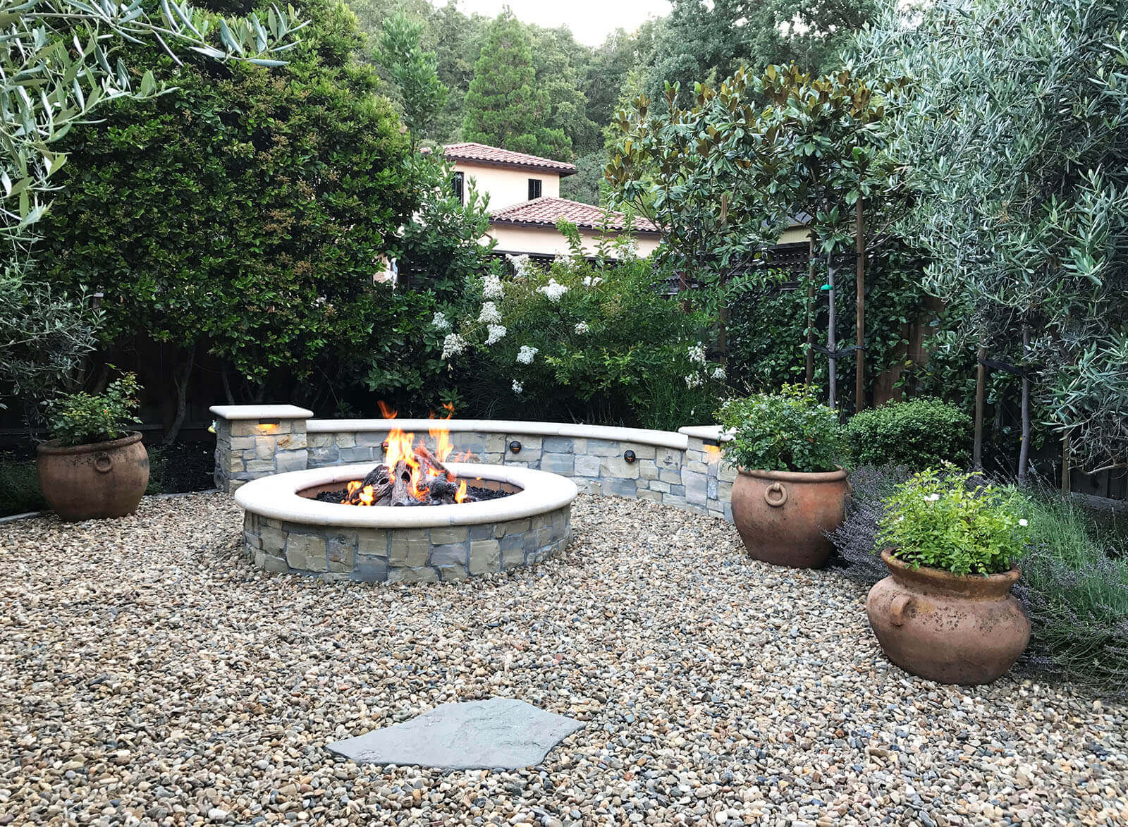 Rounded natural fireplace with stone bench and gravel surrounding area and stone walkway
