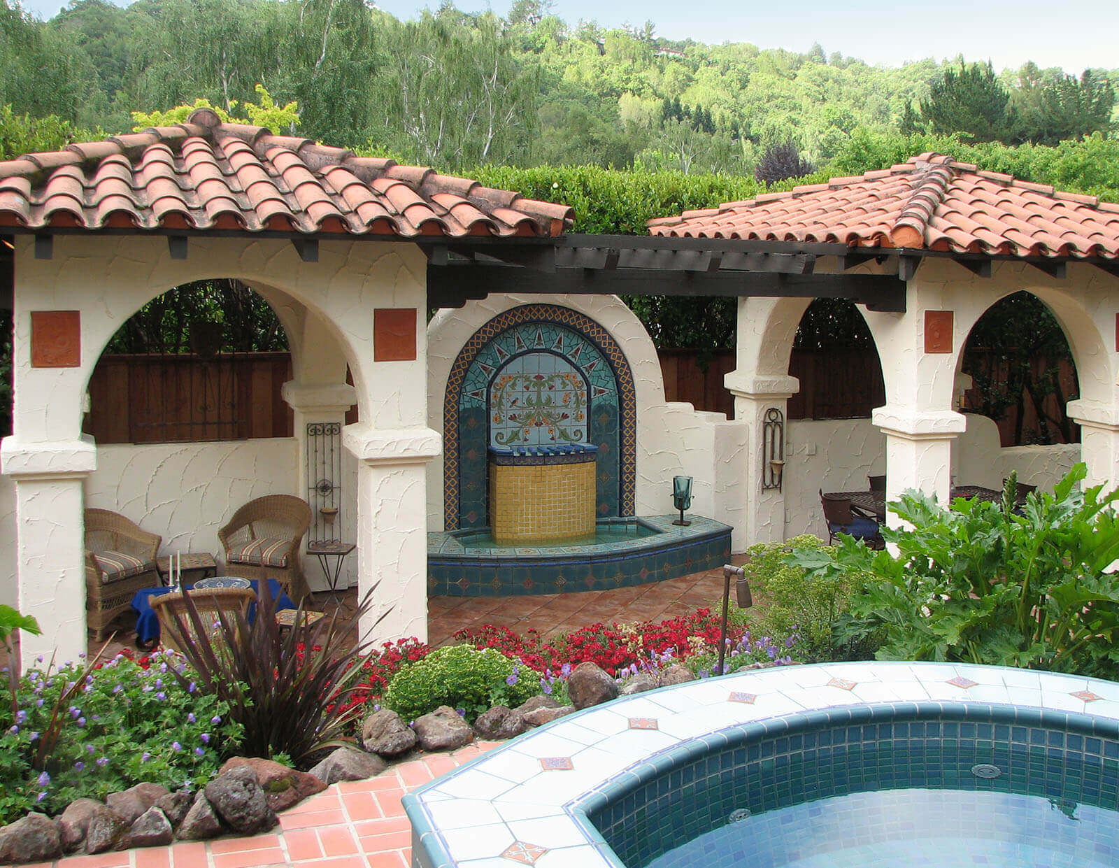 Shaded small squared mission style roof verandas connected with a dark wood pergola with arched mosaic fountain underneath