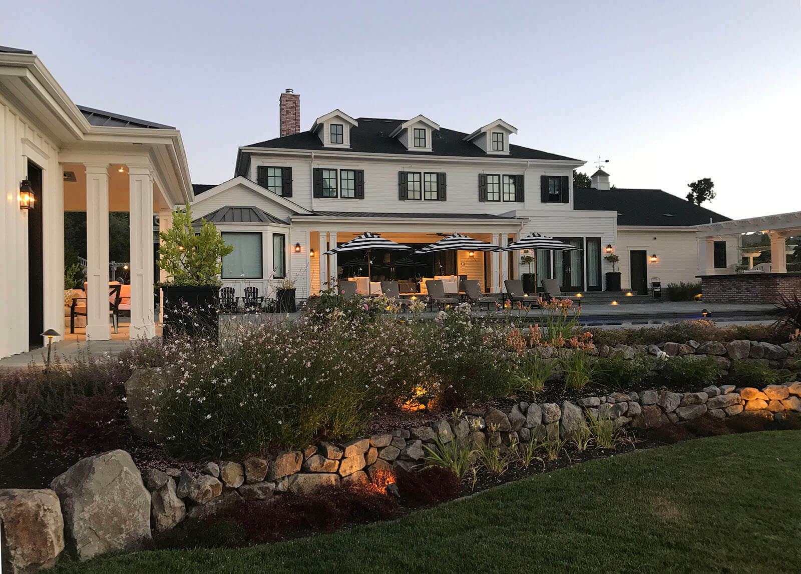 Outdoor lighting at sunset, light fixtures around the edge of the structures, and accent lighting on staged gardening areas
