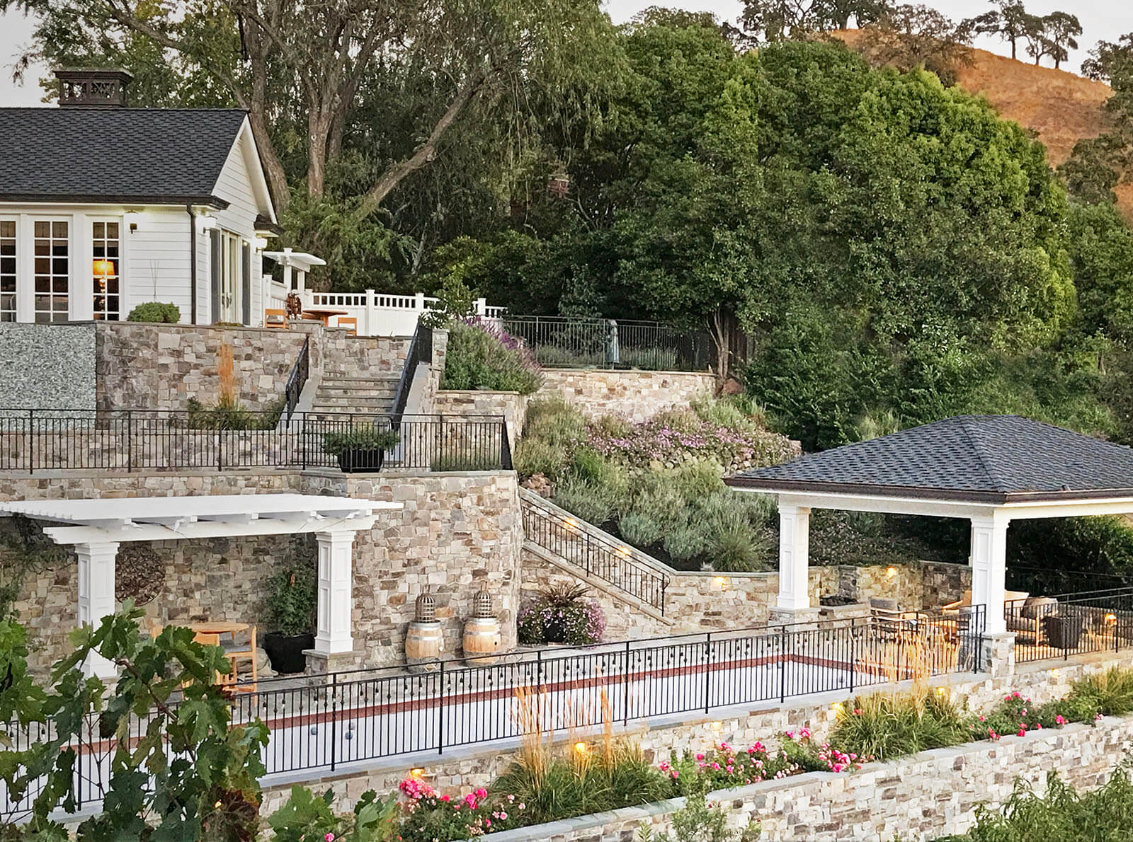 Mediterranean-style stone terrace with bocce ball court, pergola and pagoda seating